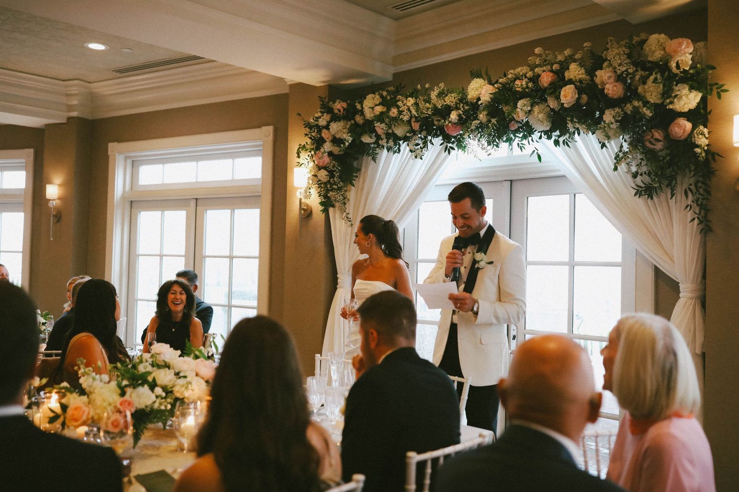 Wedding ceremony space decorated with floral arch and natural light streaming through windows.
