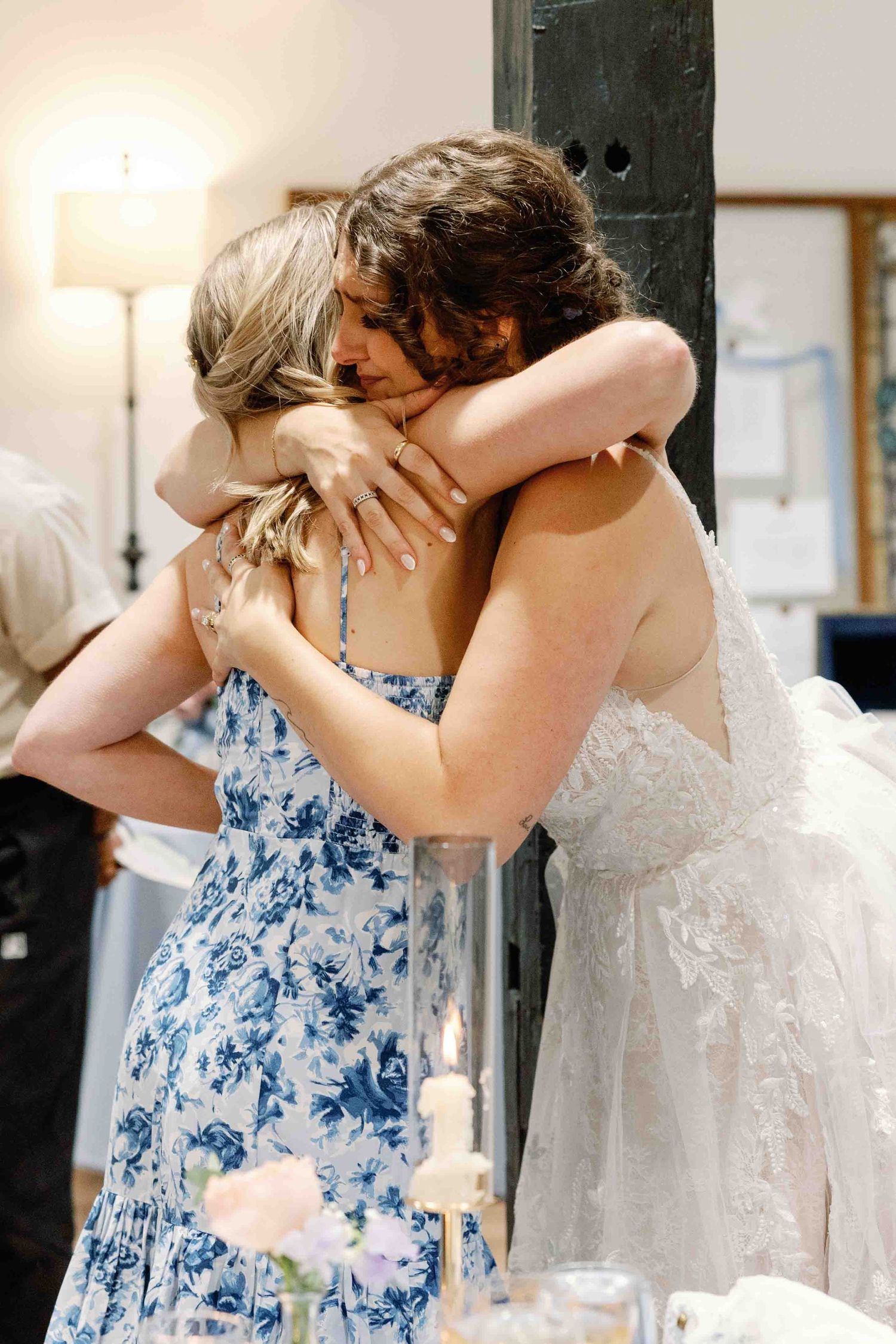 Tender moment between wedding party members in blue floral dresses and white gown.
