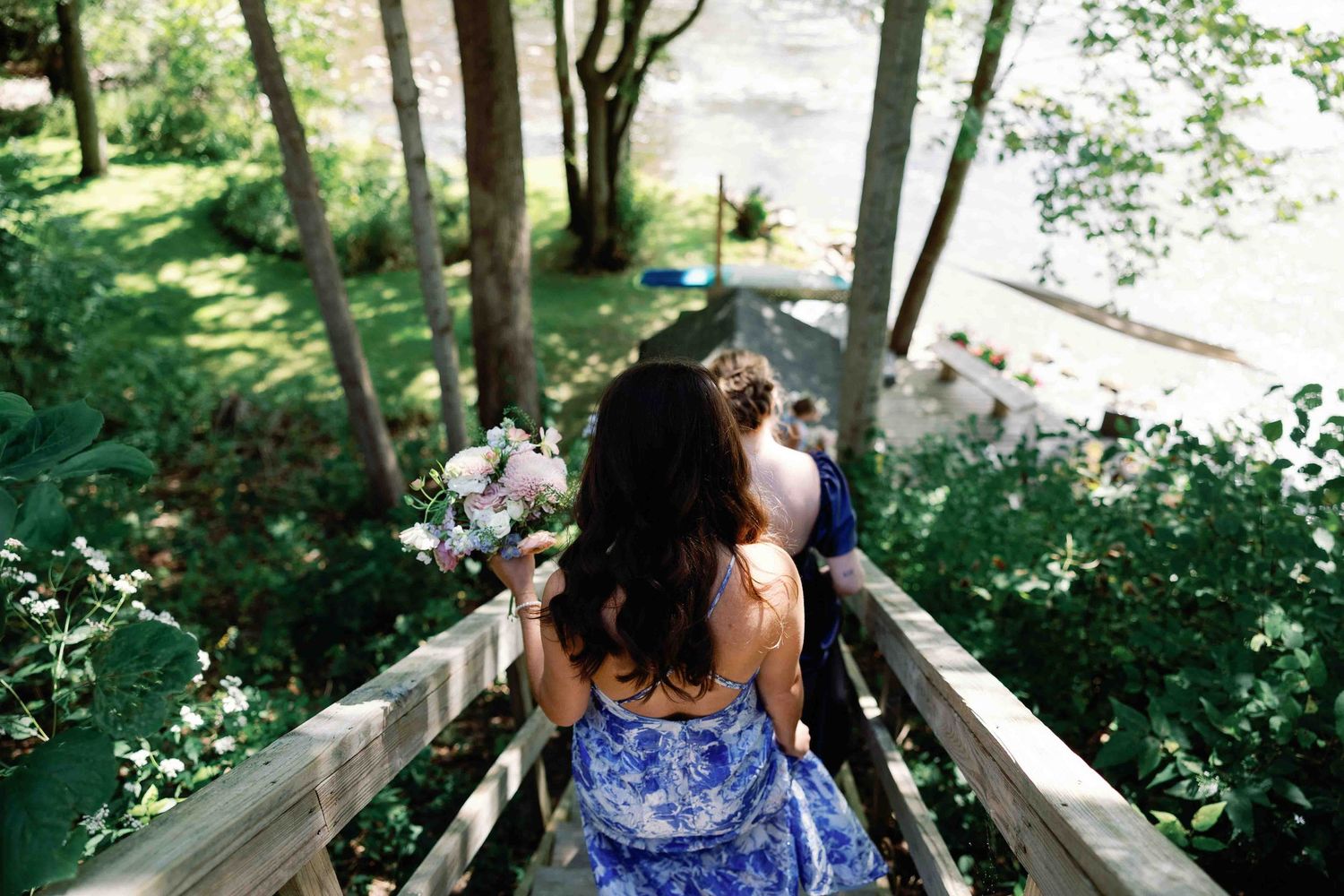 A person in a blue floral dress descends wooden stairs surrounded by lush greenery.