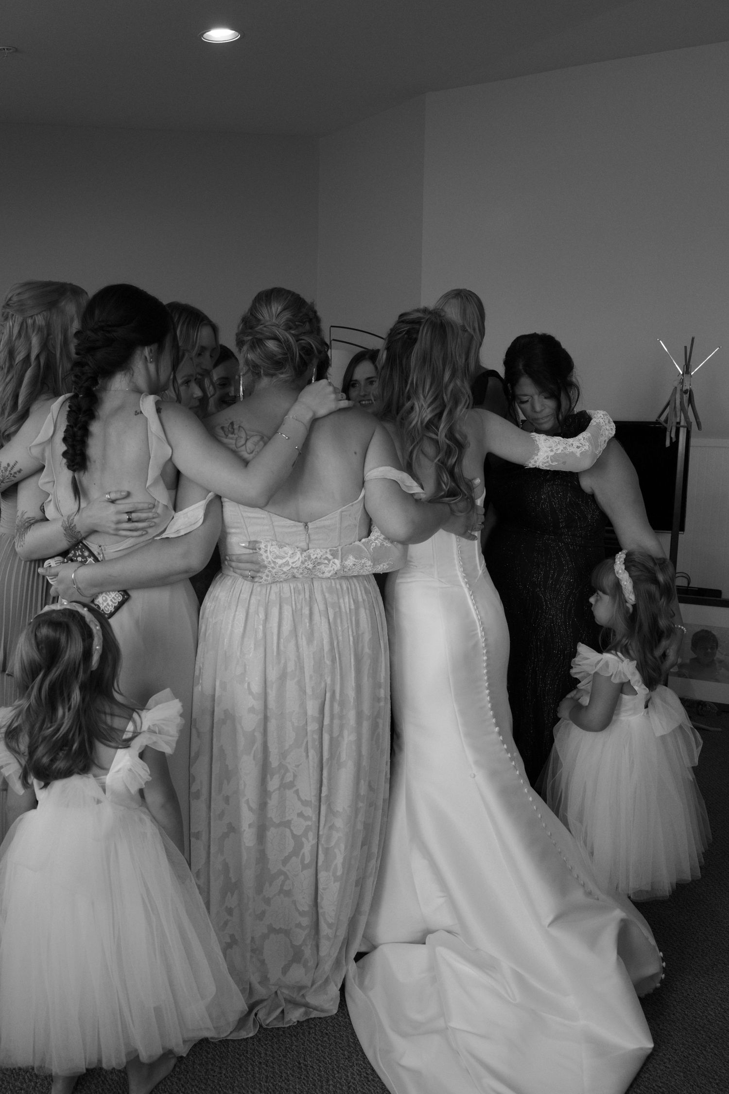 A group poses together in elegant white and cream colored formal dresses in an indoor setting.