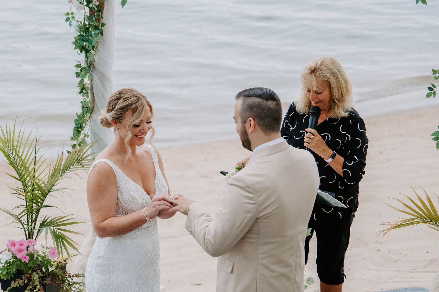 Seaside wedding ceremony with elegant white draping and tropical greenery decorations.