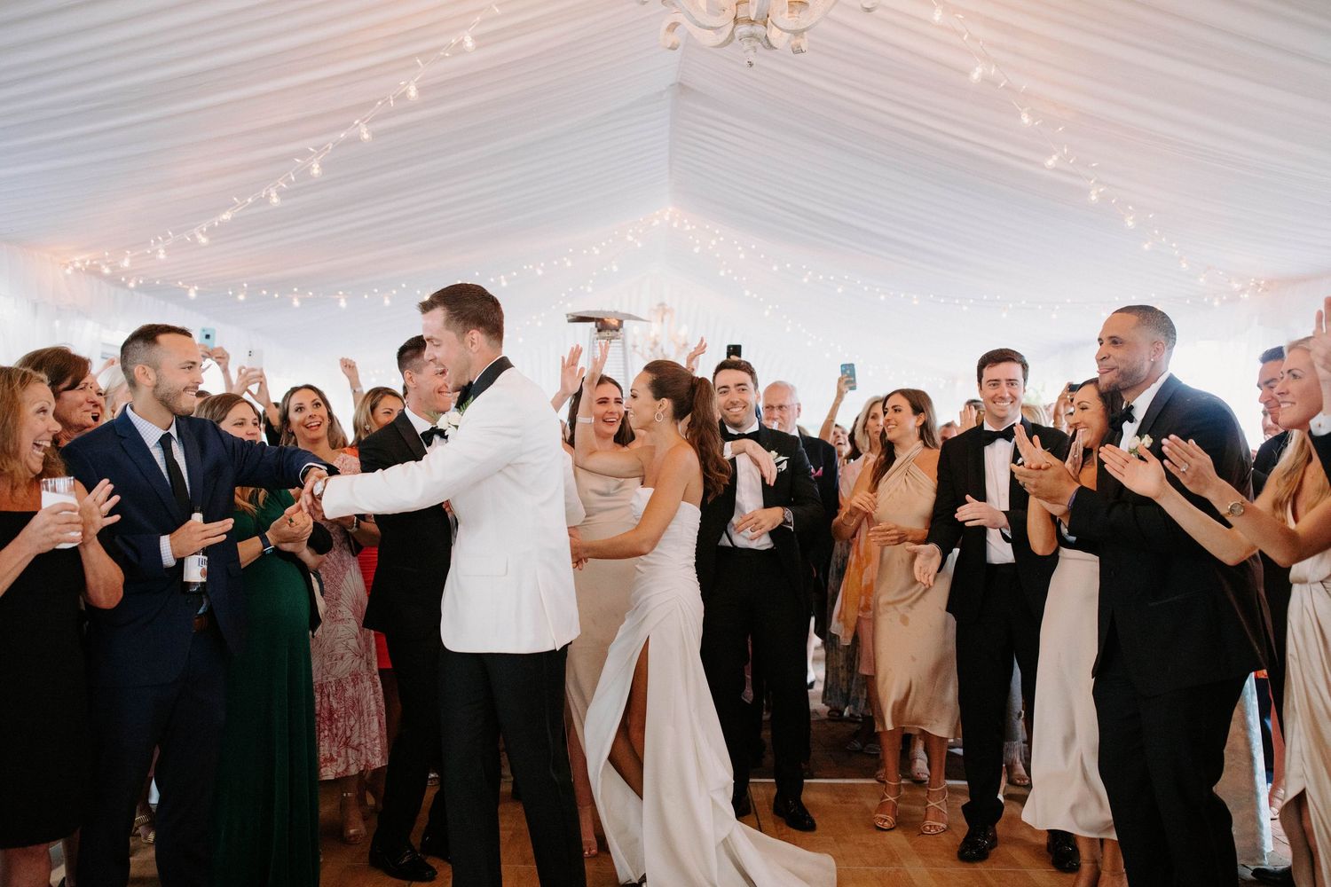 Wedding guests dancing and celebrating in a tent with string lights.