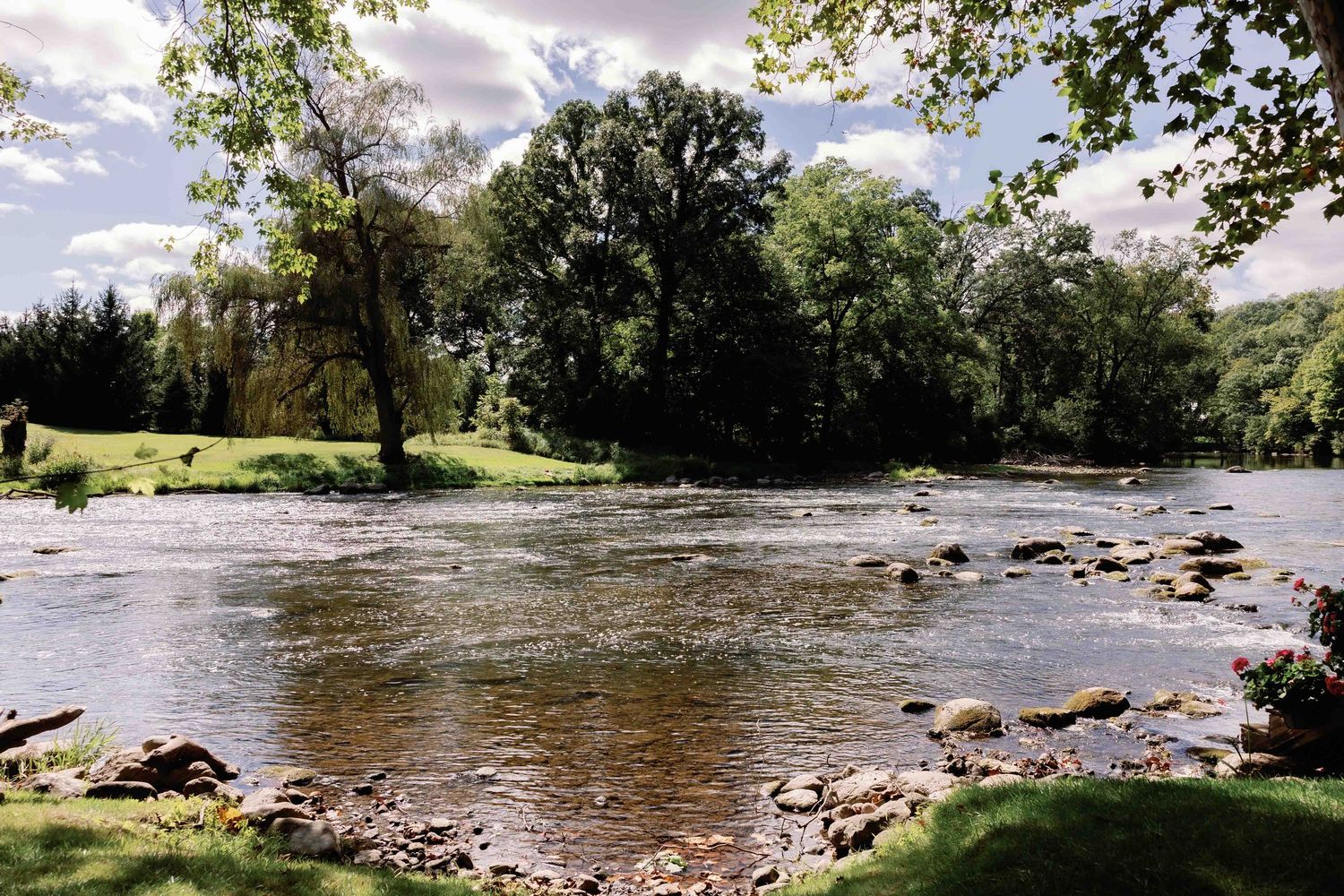 Scenic river landscape with rocky shores and trees under a cloudy summer sky.