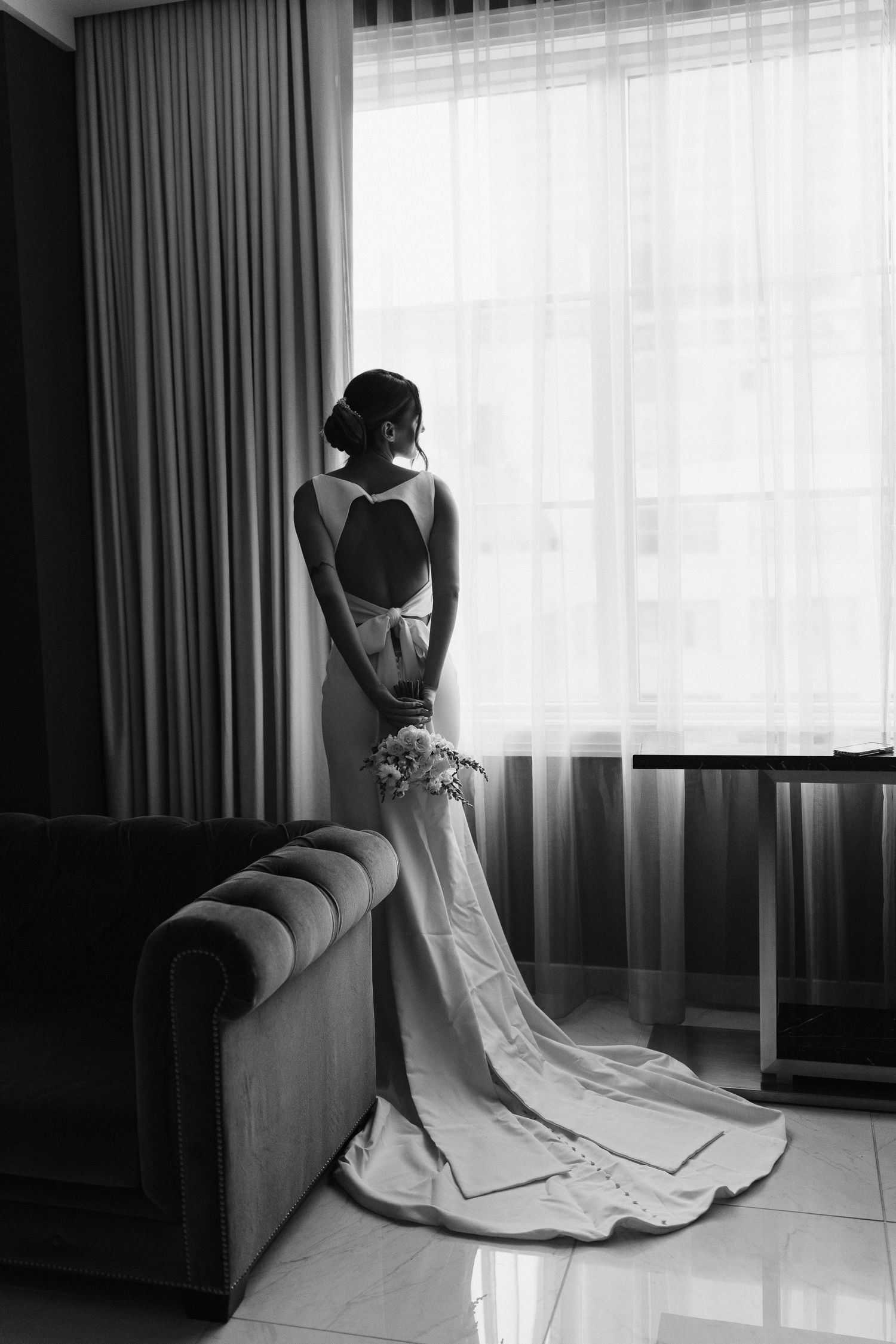 Artistic black and white bridal portraits showcasing detailed wedding gown in hotel room setting.