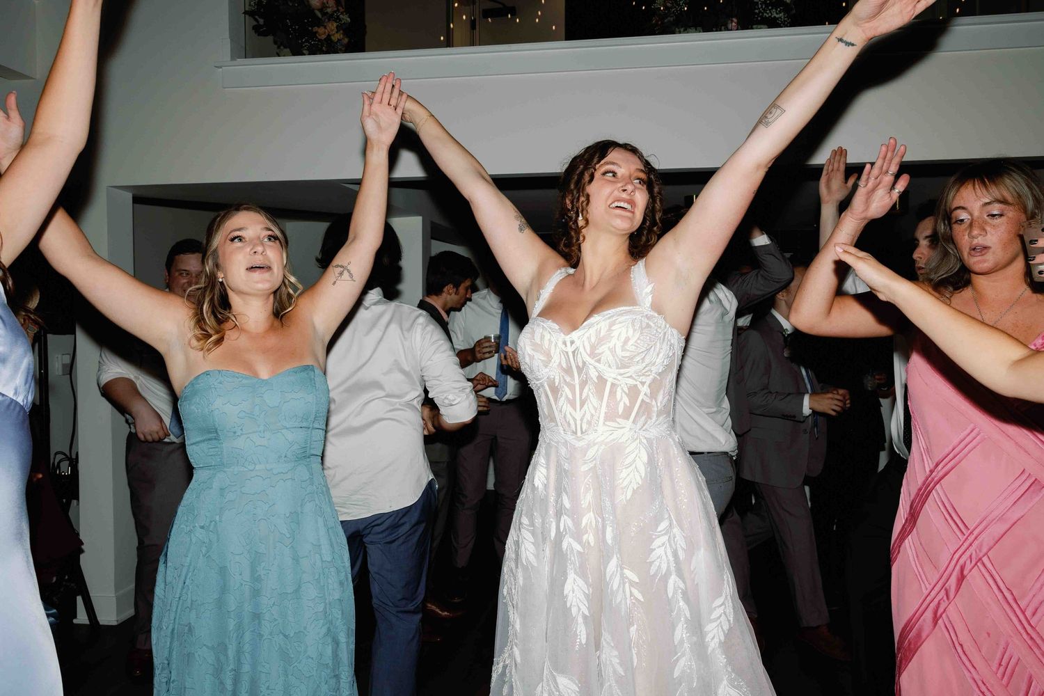Wedding party guests dancing energetically on a dance floor in blue and pink dresses.
