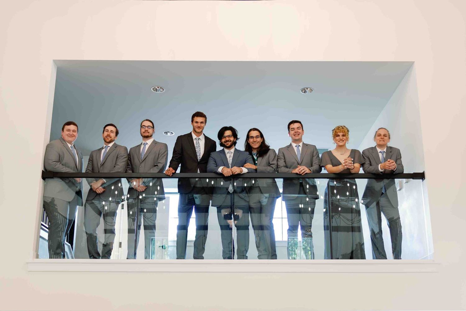 Professional group photo of business team standing together against light colored wall.