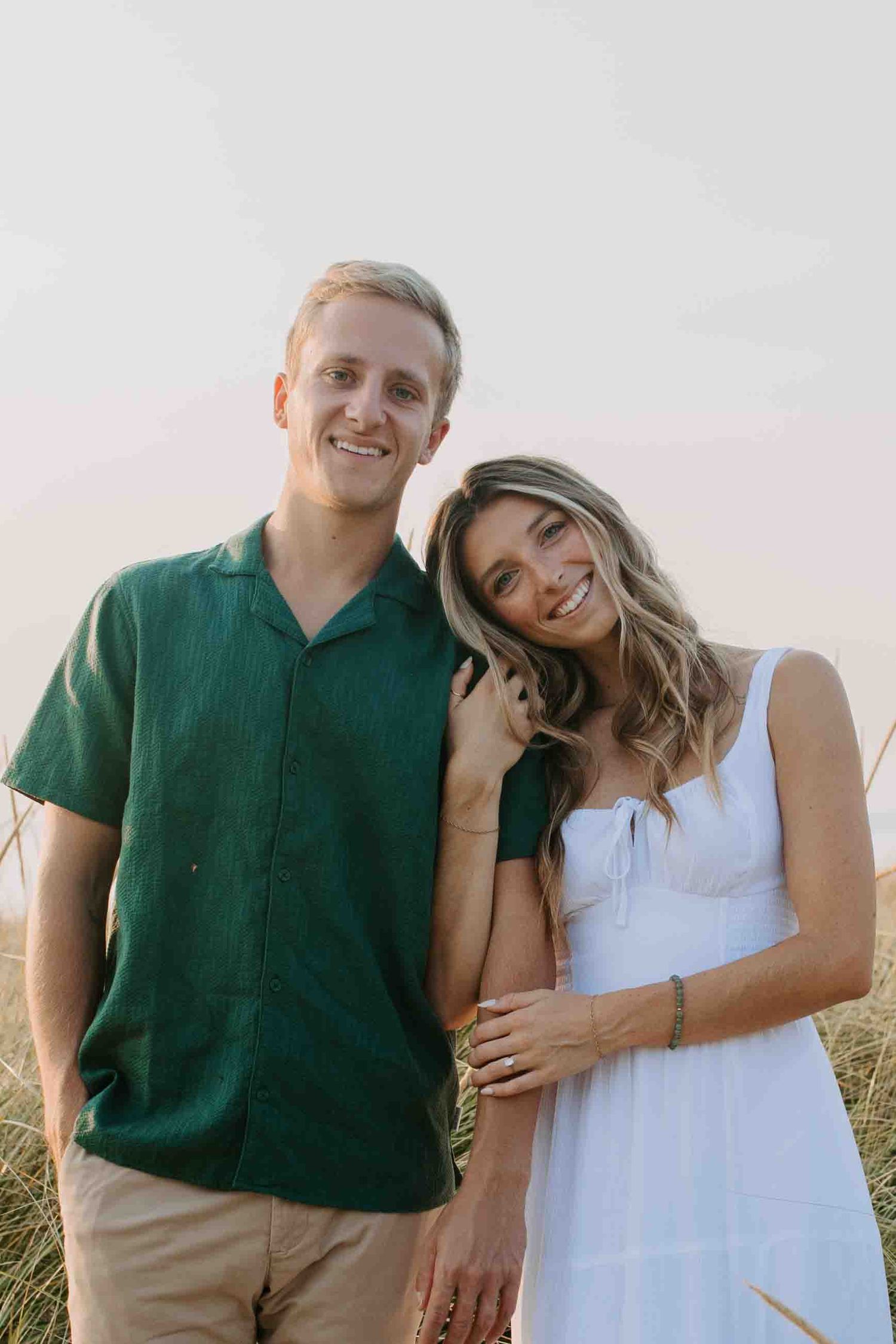 Couple in casual summer outfits taking sunset portraits in a field.