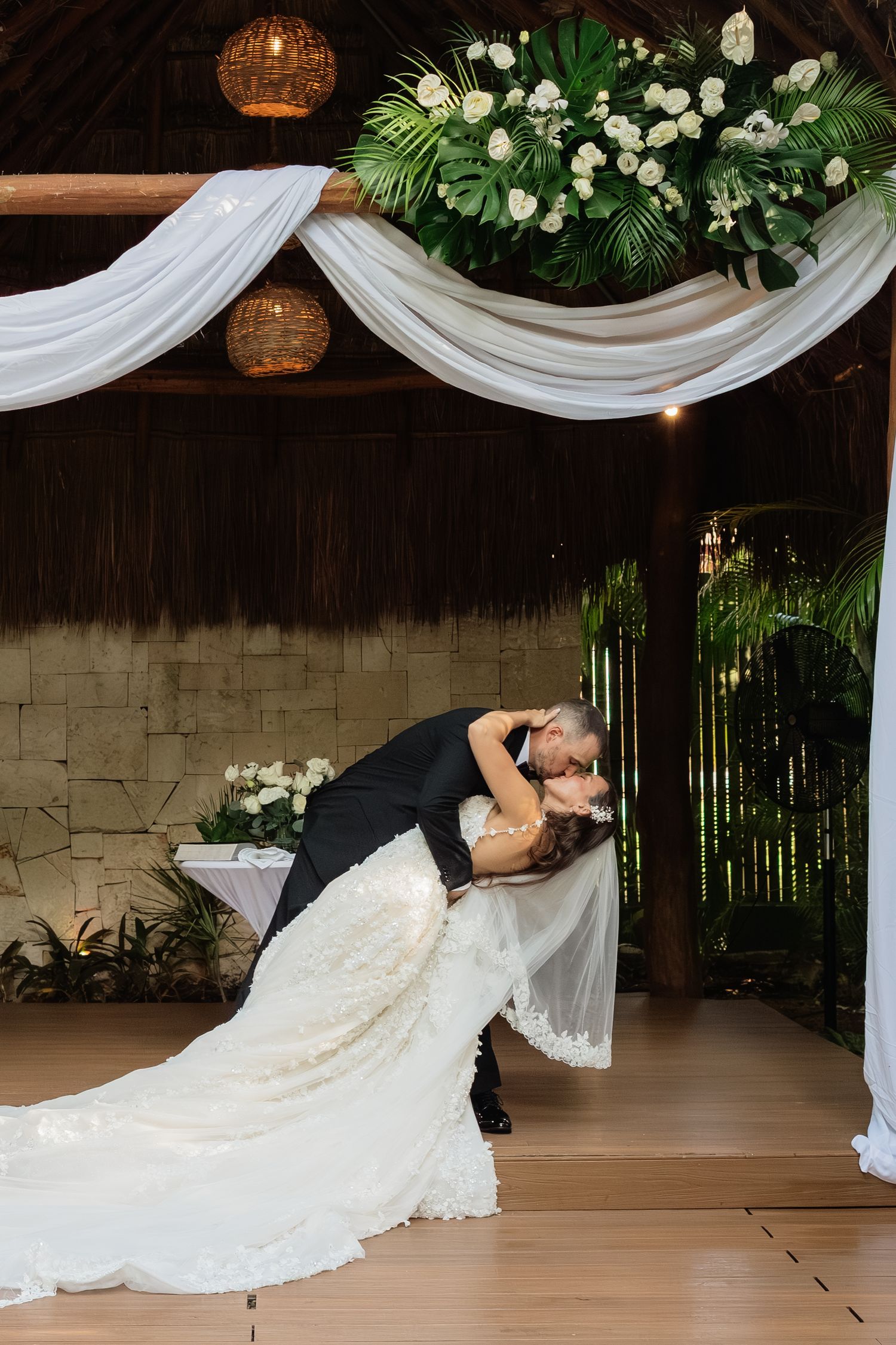 Romantic dance dip pose under white drapery and floral decorations.