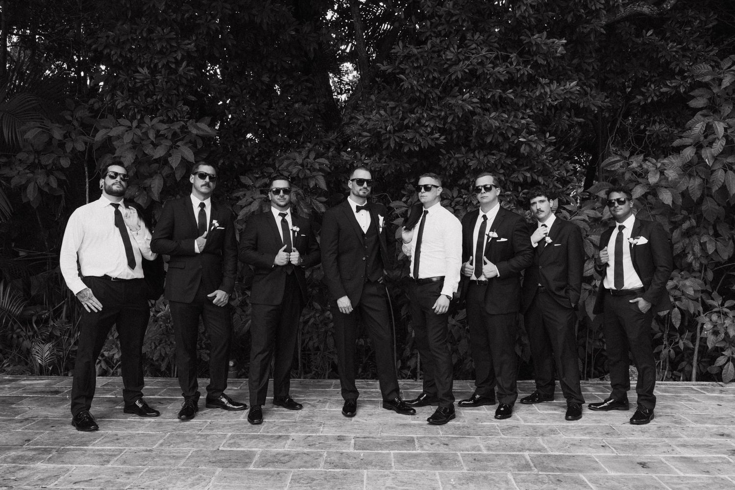 Groomsmen in black suits jumping in sequence on outdoor steps for a fun wedding photo.