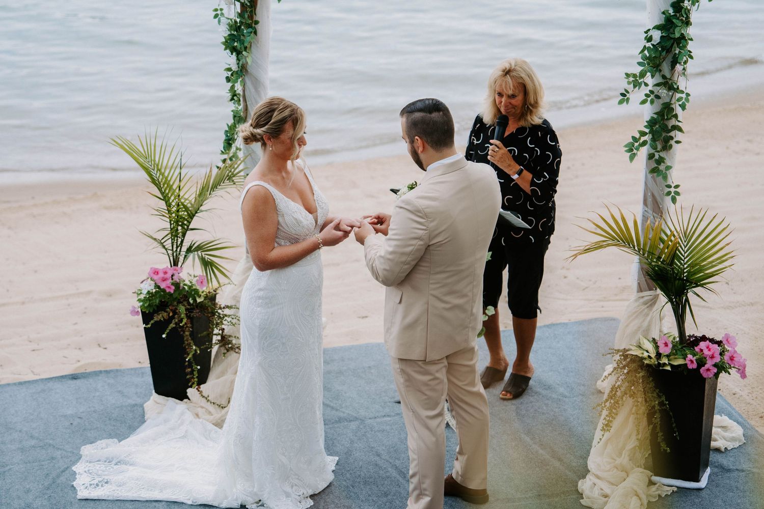 Wedding ceremony taking place on a waterfront deck with tropical greenery decorations.