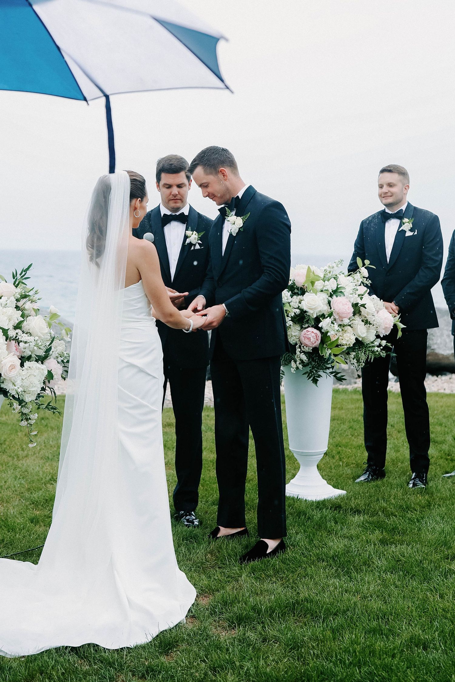 Wedding ceremony exchange on grass with formal attire and elegant white floral decor.