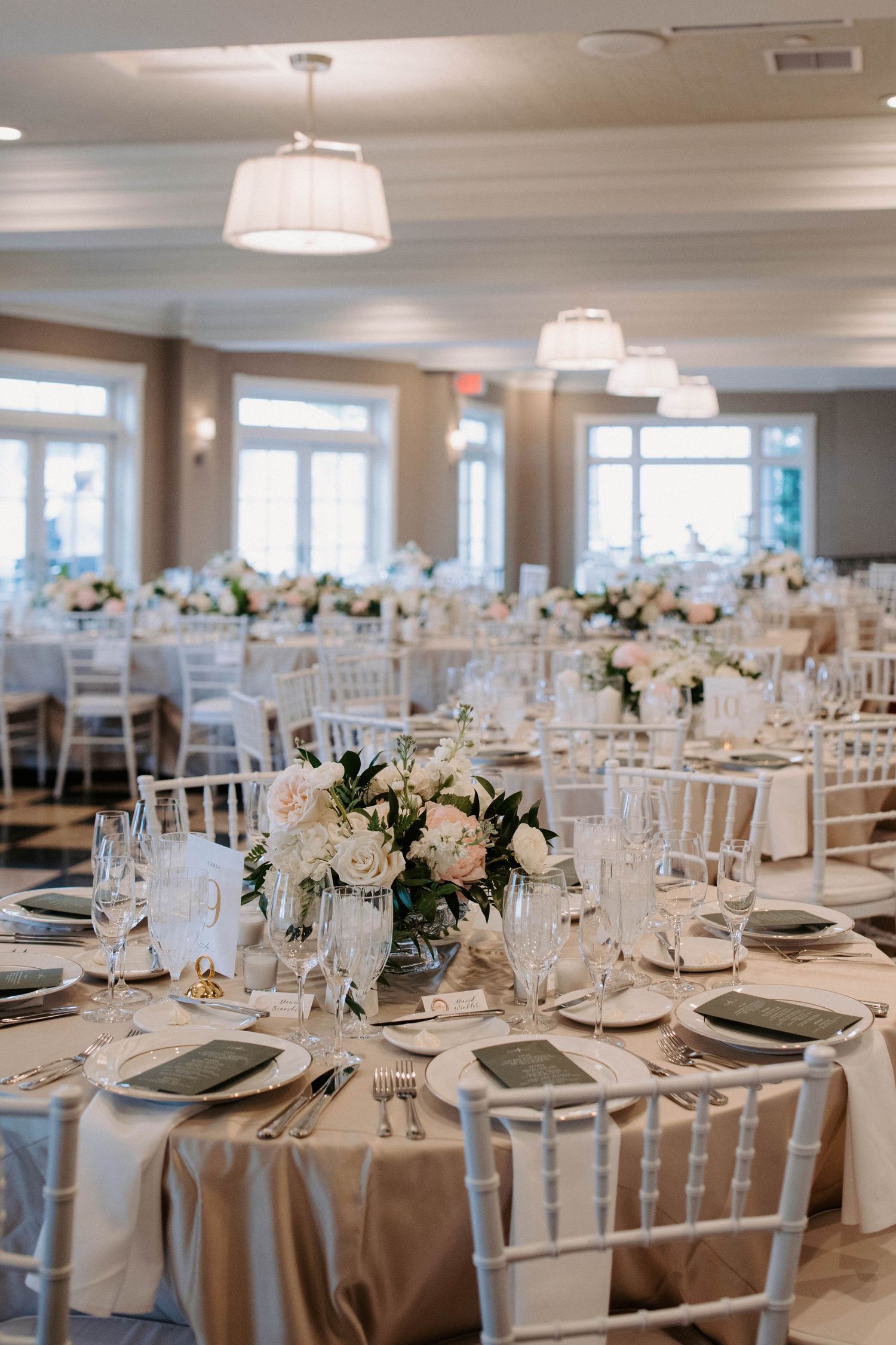 A bright reception hall with round tables decorated with white linens and floral centerpieces.