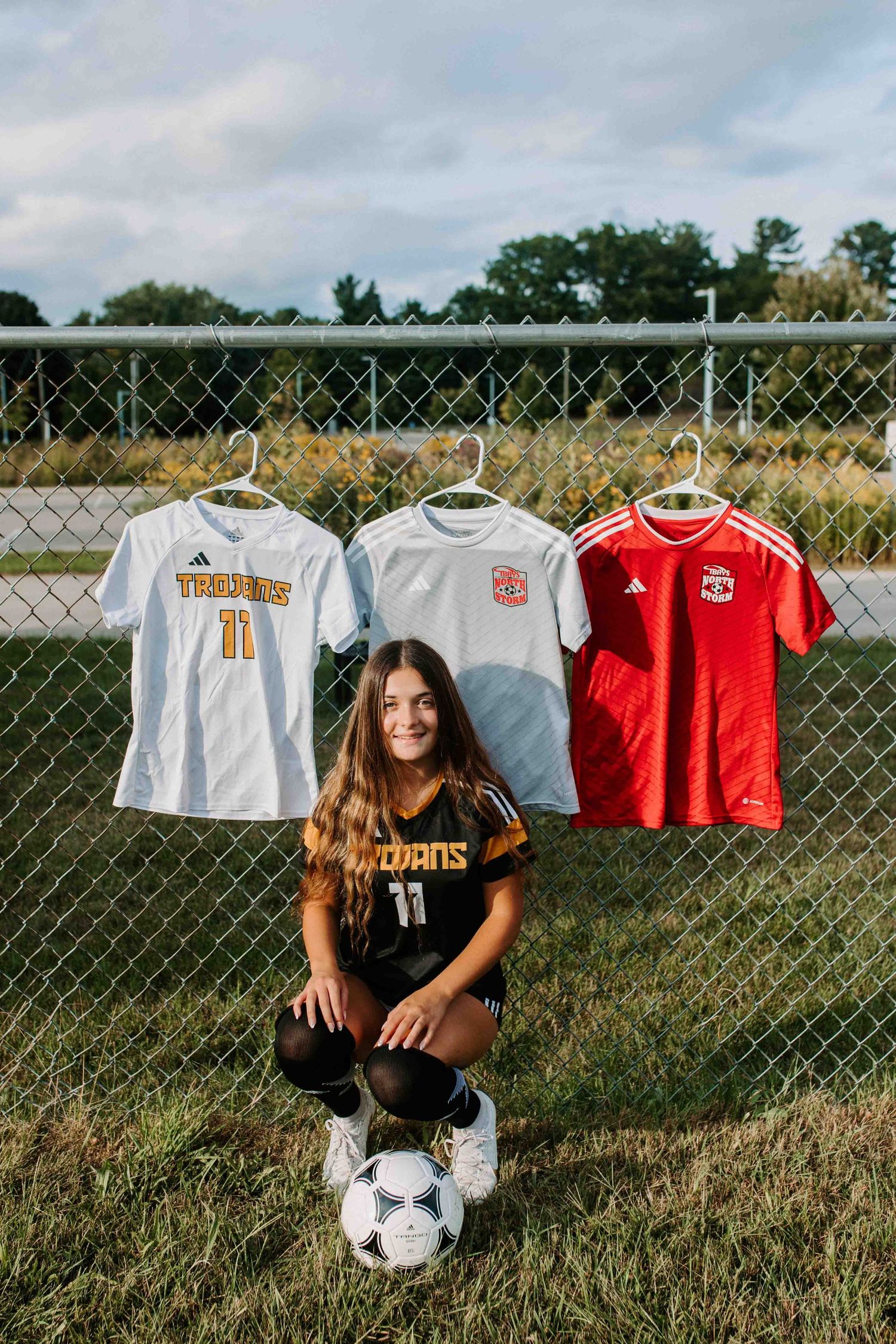 Soccer jerseys displayed on fence with player posing on field.