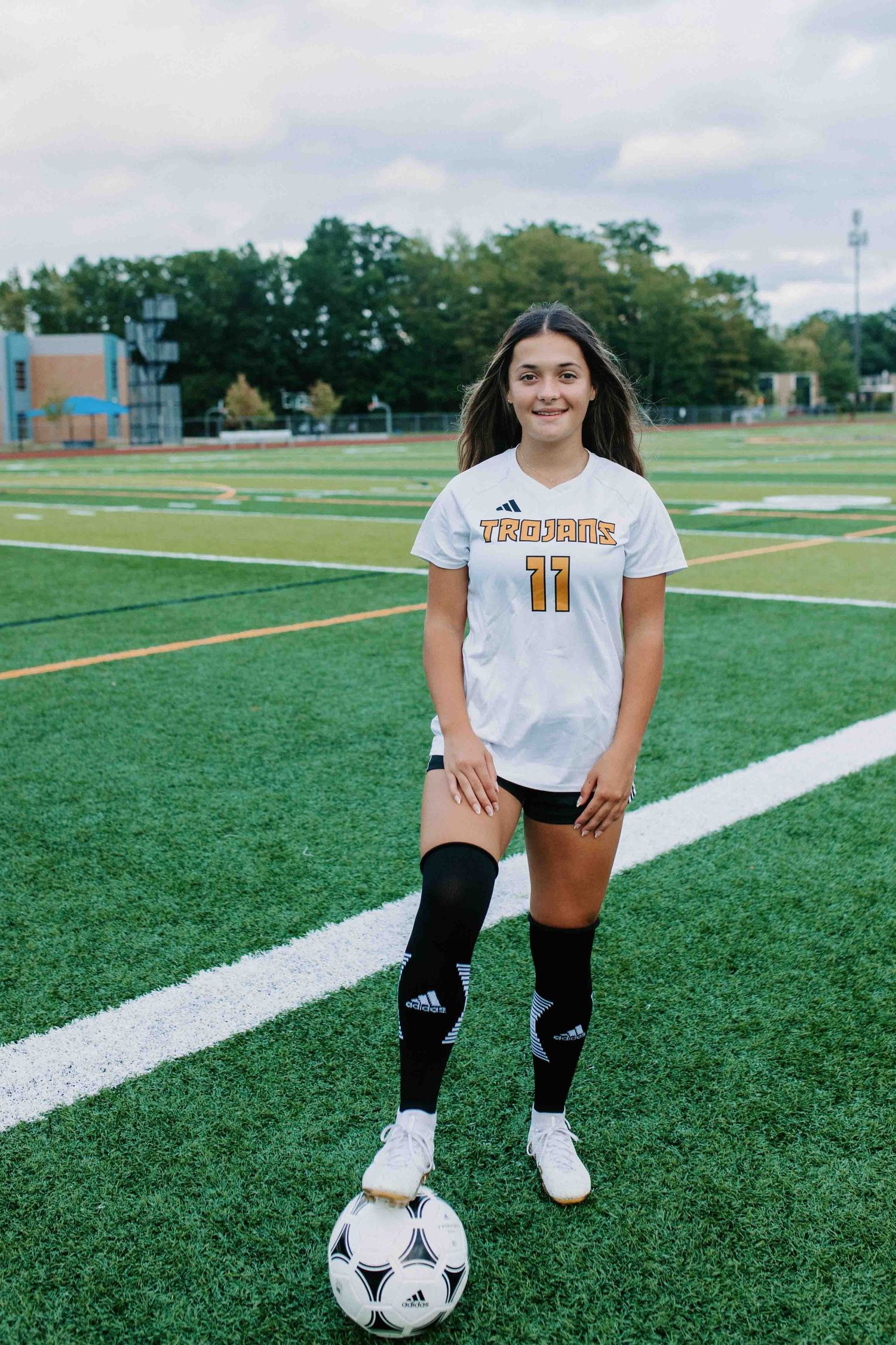 Soccer player in white Trojans jersey poses with ball on green turf field.