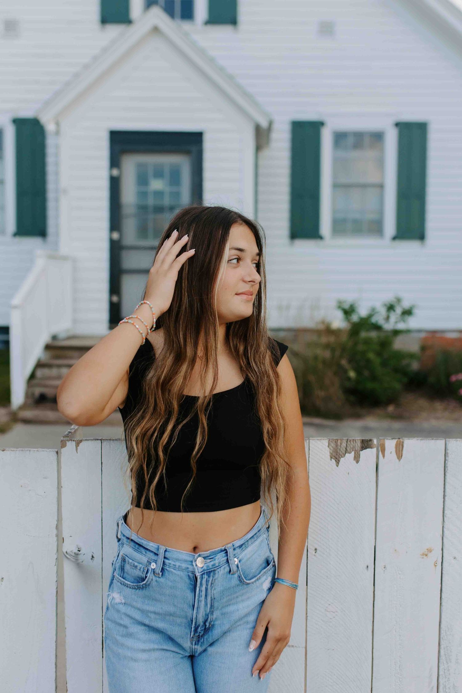 Relaxed poses against white picket fence with classic farmhouse setting.