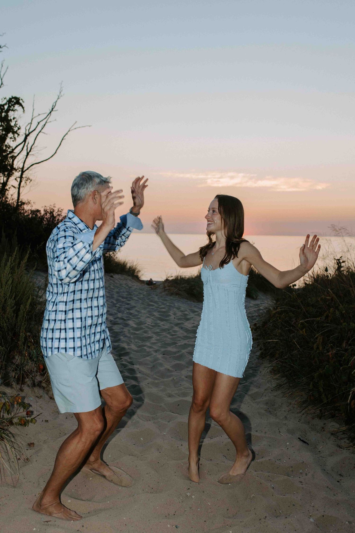 People playfully dancing and jumping on a beach trail during golden hour.