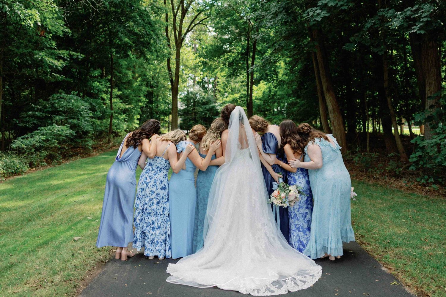 Wedding party in coordinated blue dresses walks together on an outdoor path.