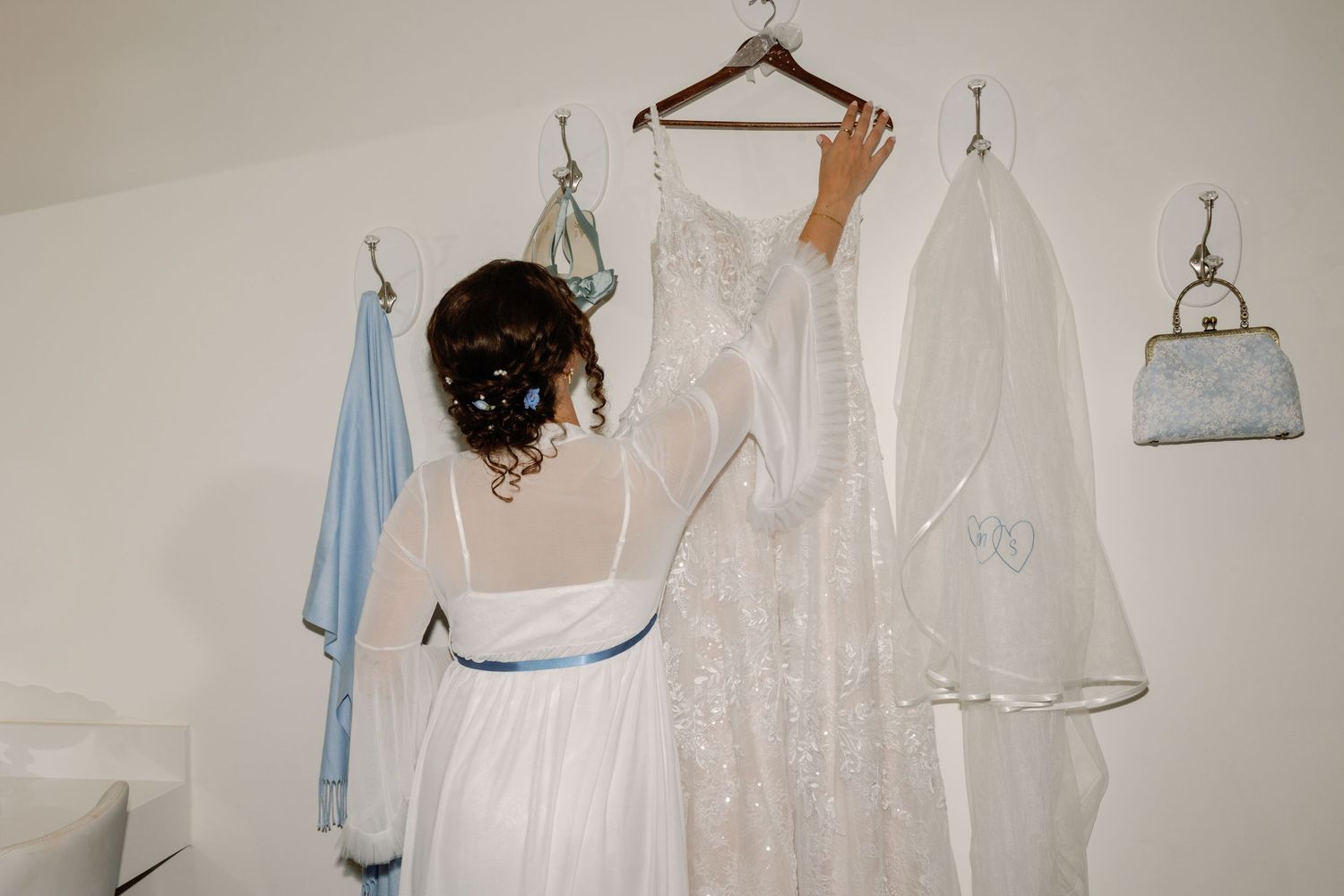 White wedding dresses and formal attire hanging on wooden hangers against a neutral wall.