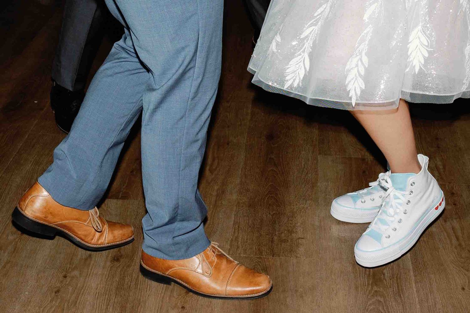 Close-up of various wedding guests' shoes and feet on a wooden dance floor.