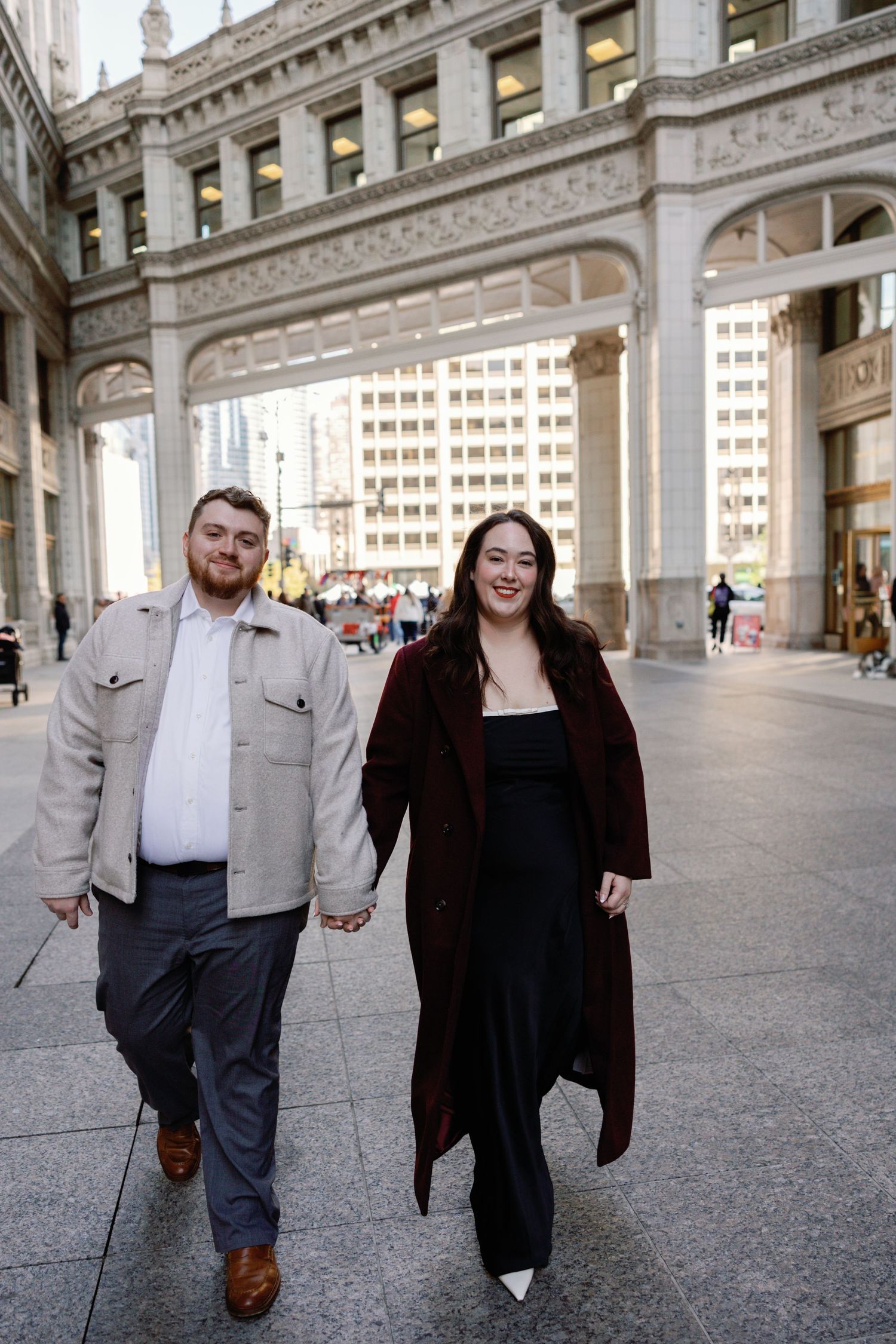 A couple walks together through an elegant colonnade with classical architecture.