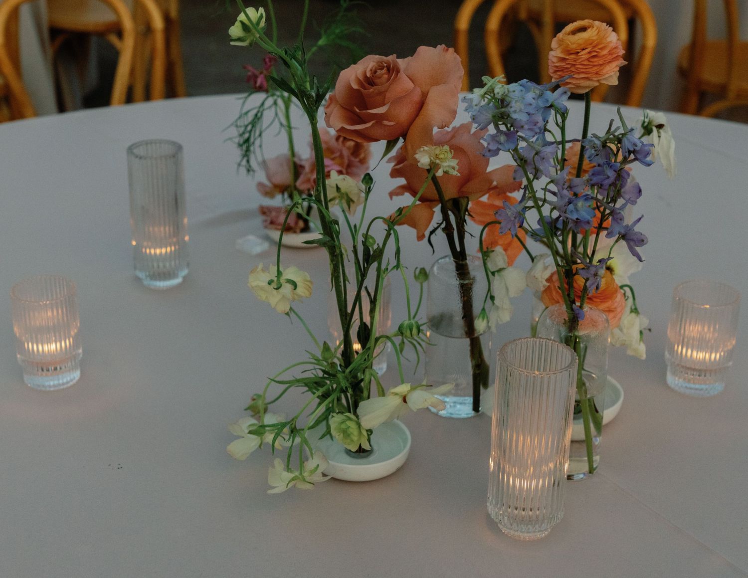 Elegant table settings with delicate floral centerpieces and glass candle holders at a wedding reception.
