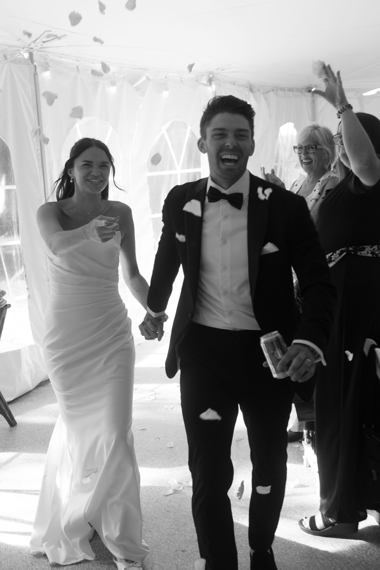 Wedding party runs joyfully through a white tent during celebration festivities.