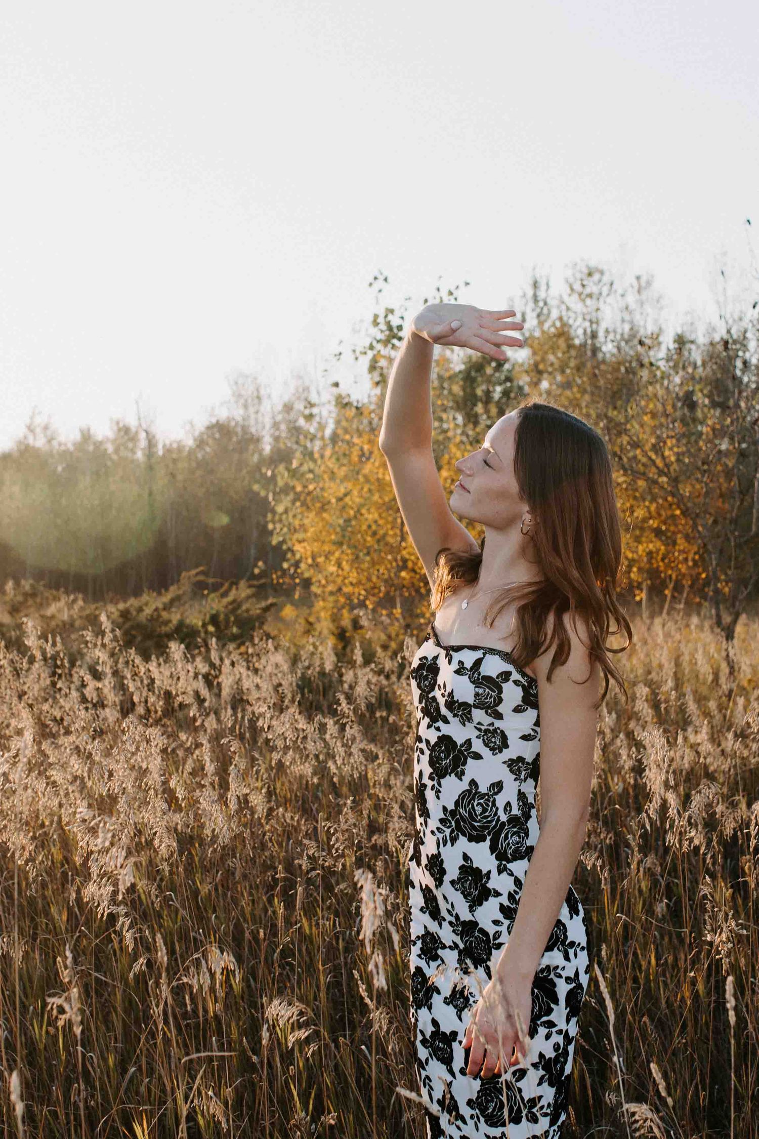 A floral black and white dress contrasts beautifully against golden autumn grass and sunset lighting.