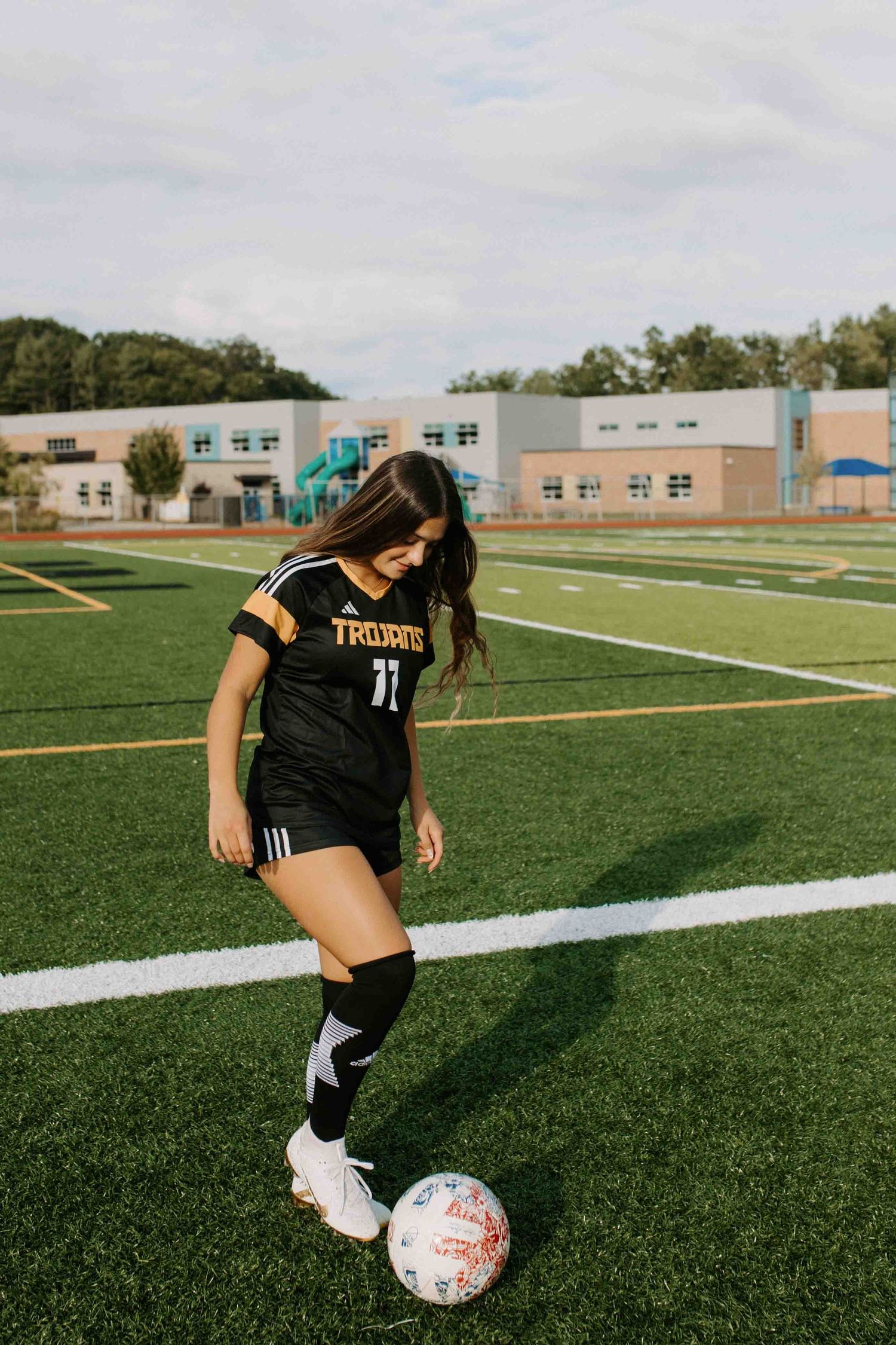 Soccer player dribbles ball on turf field wearing black Trojans uniform number 11.