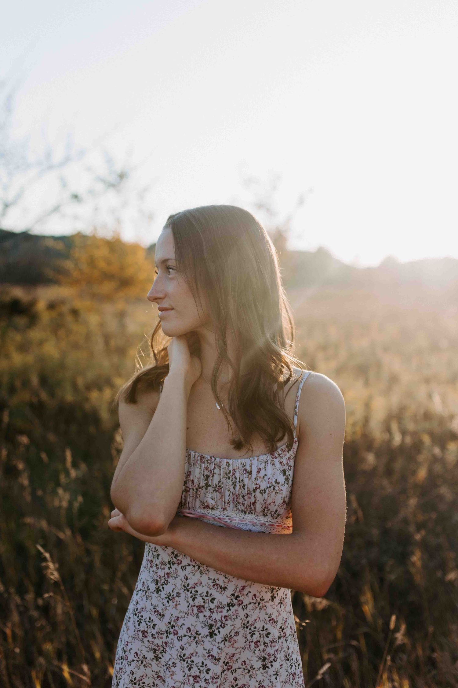 A floral sundress-clad figure stands thoughtfully in a golden field at sunset.