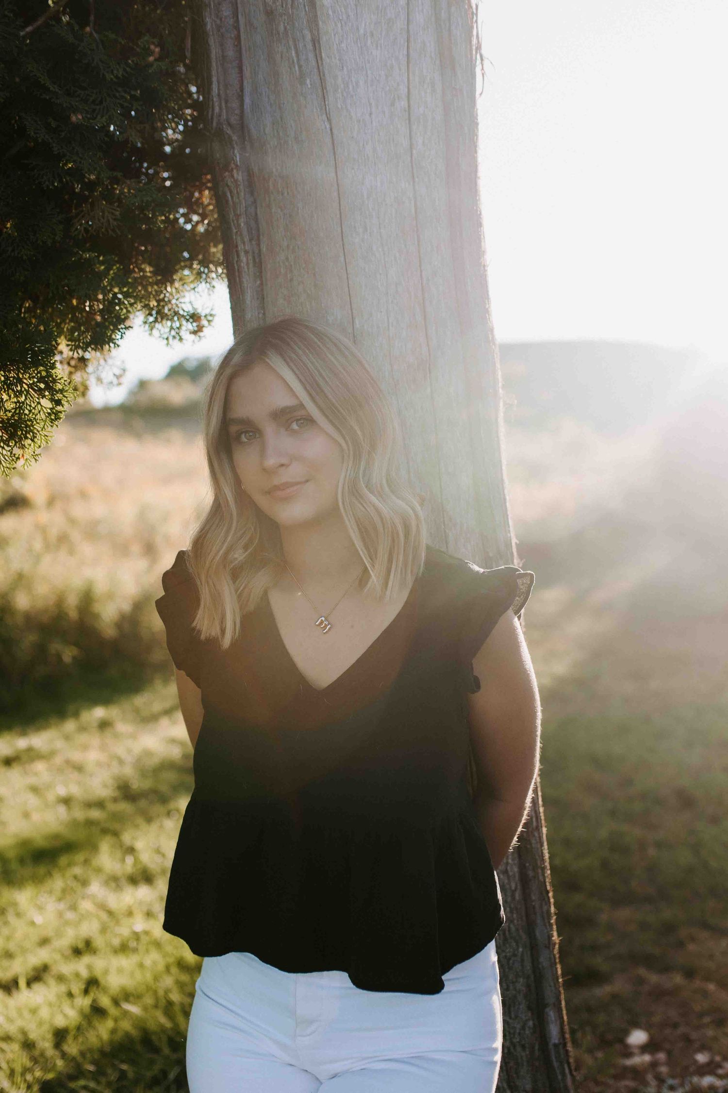 Sun-drenched outdoor portrait with black top and white pants in golden light.