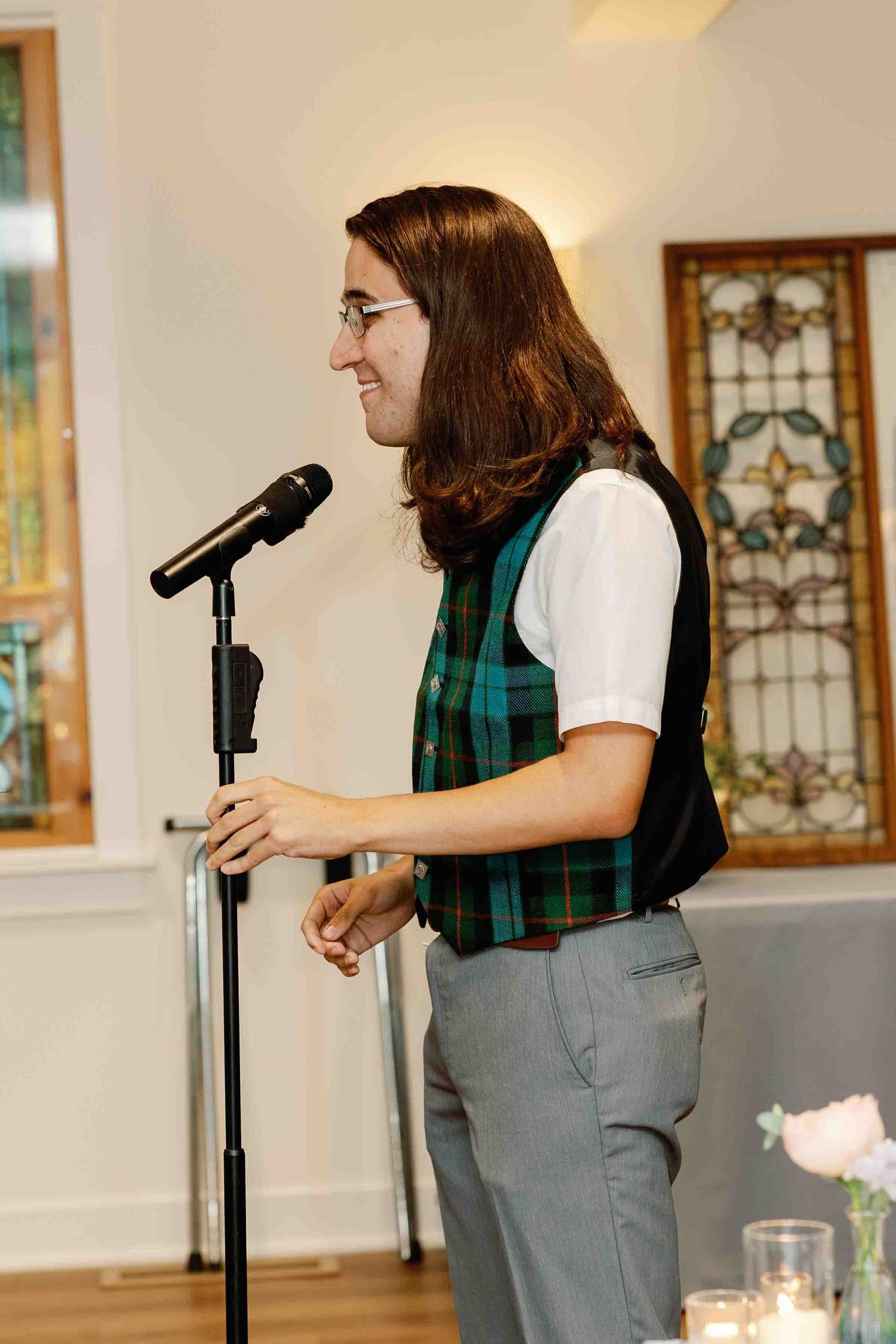 Wedding speaker delivers a heartfelt speech at the reception while wearing a plaid scarf and grey vest.