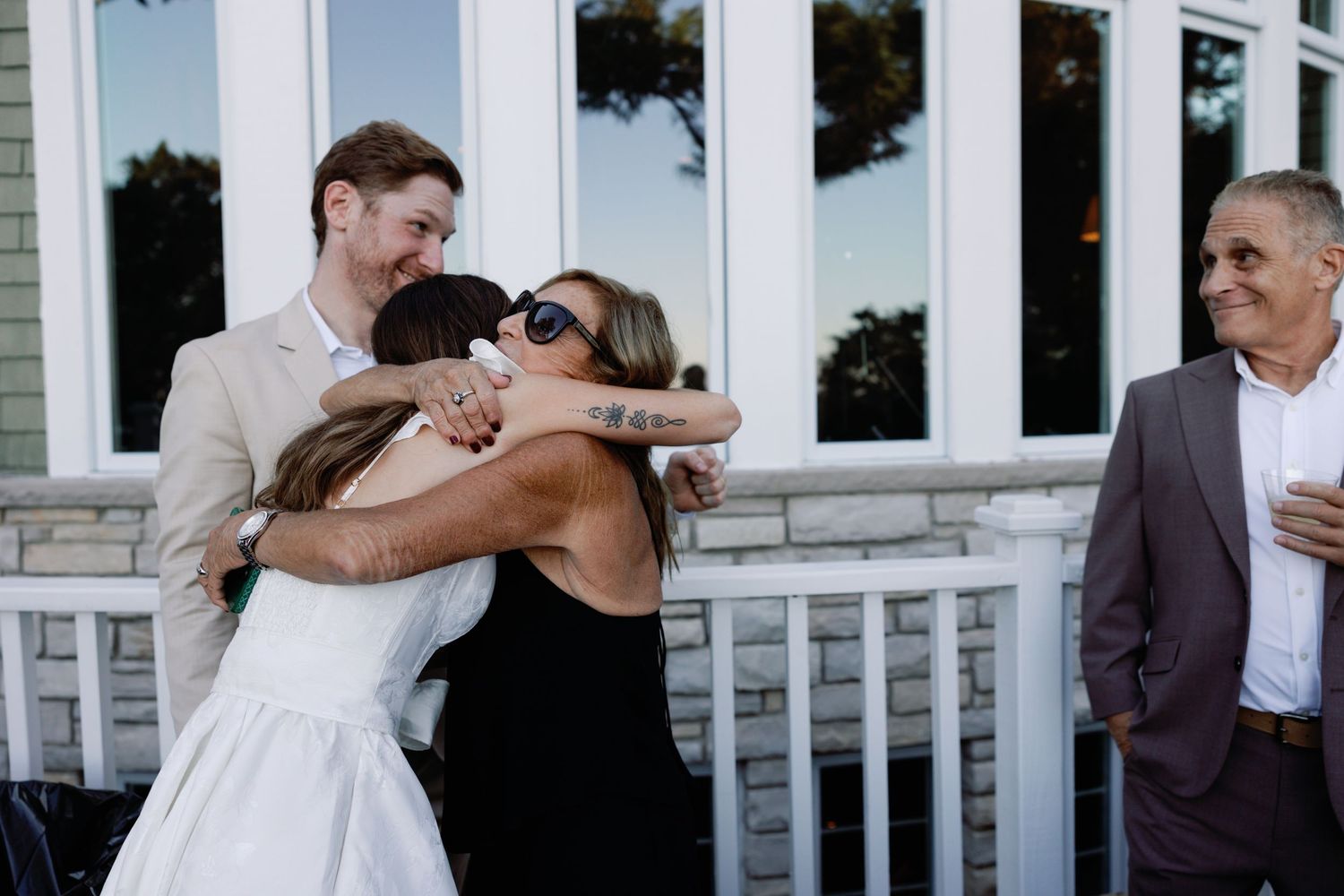 Wedding party members celebrate together on a white porch during sunset.