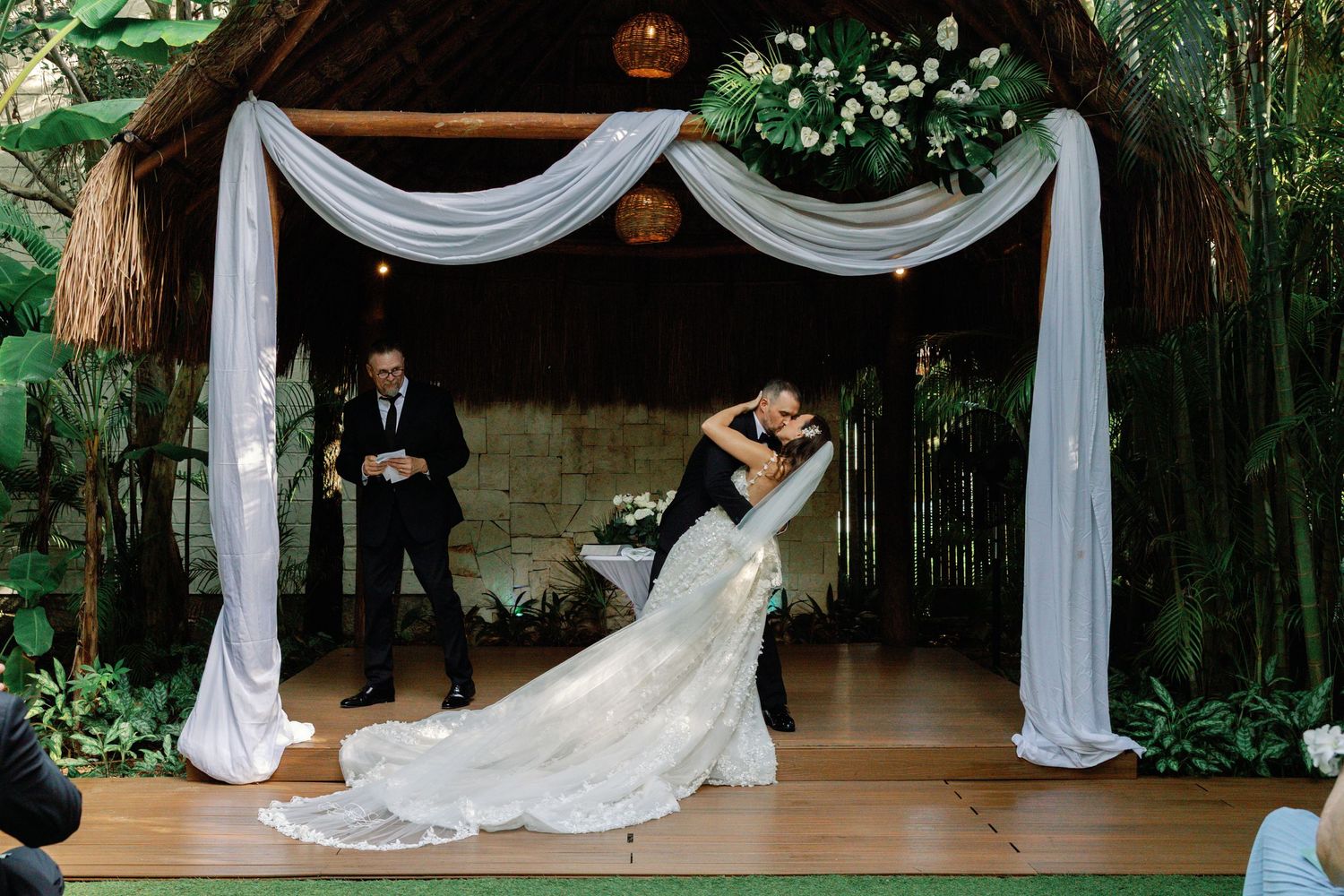 Wedding ceremony space decorated with white draping and floral arrangements in garden setting.