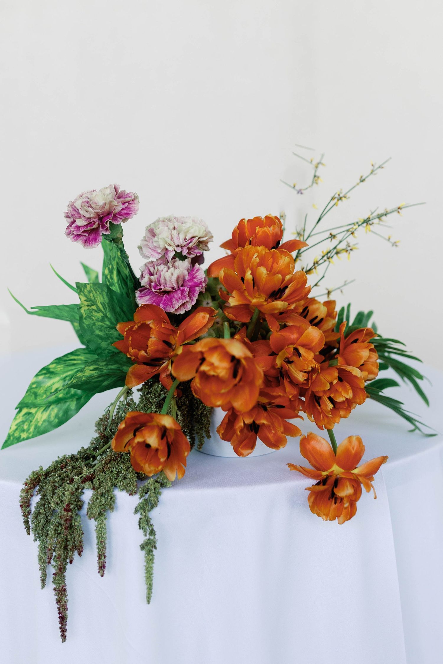 Floral arrangement featuring orange orchids and pink flowers with green foliage against white background.