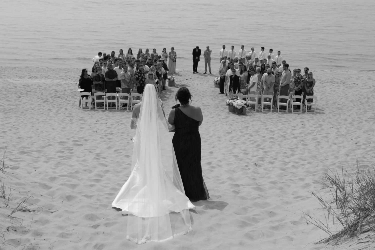 Beach wedding ceremony setup with rows of chairs and guests gathering by the water.