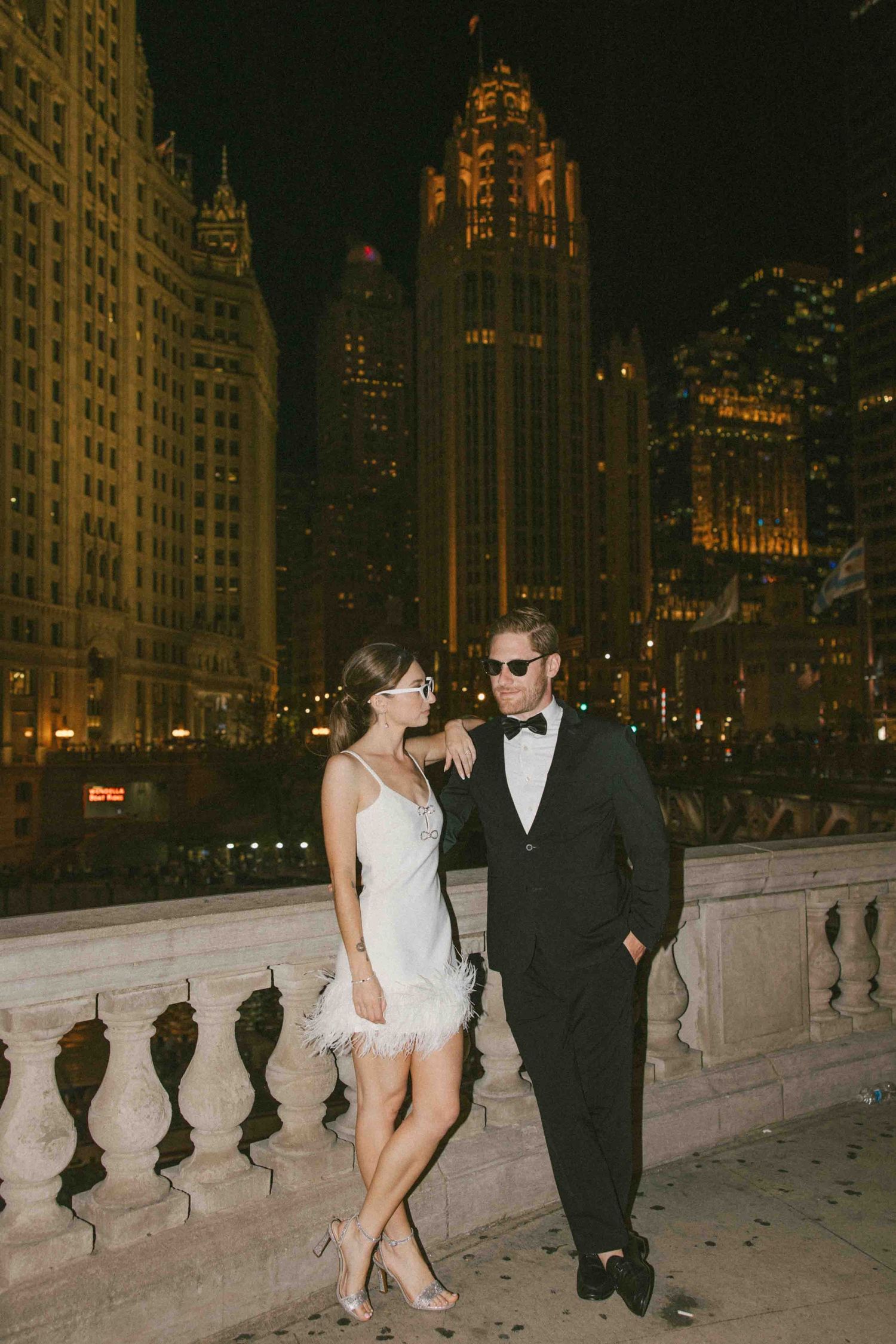 A couple shares an intimate moment on a bridge overlooking the Chicago skyline at night.