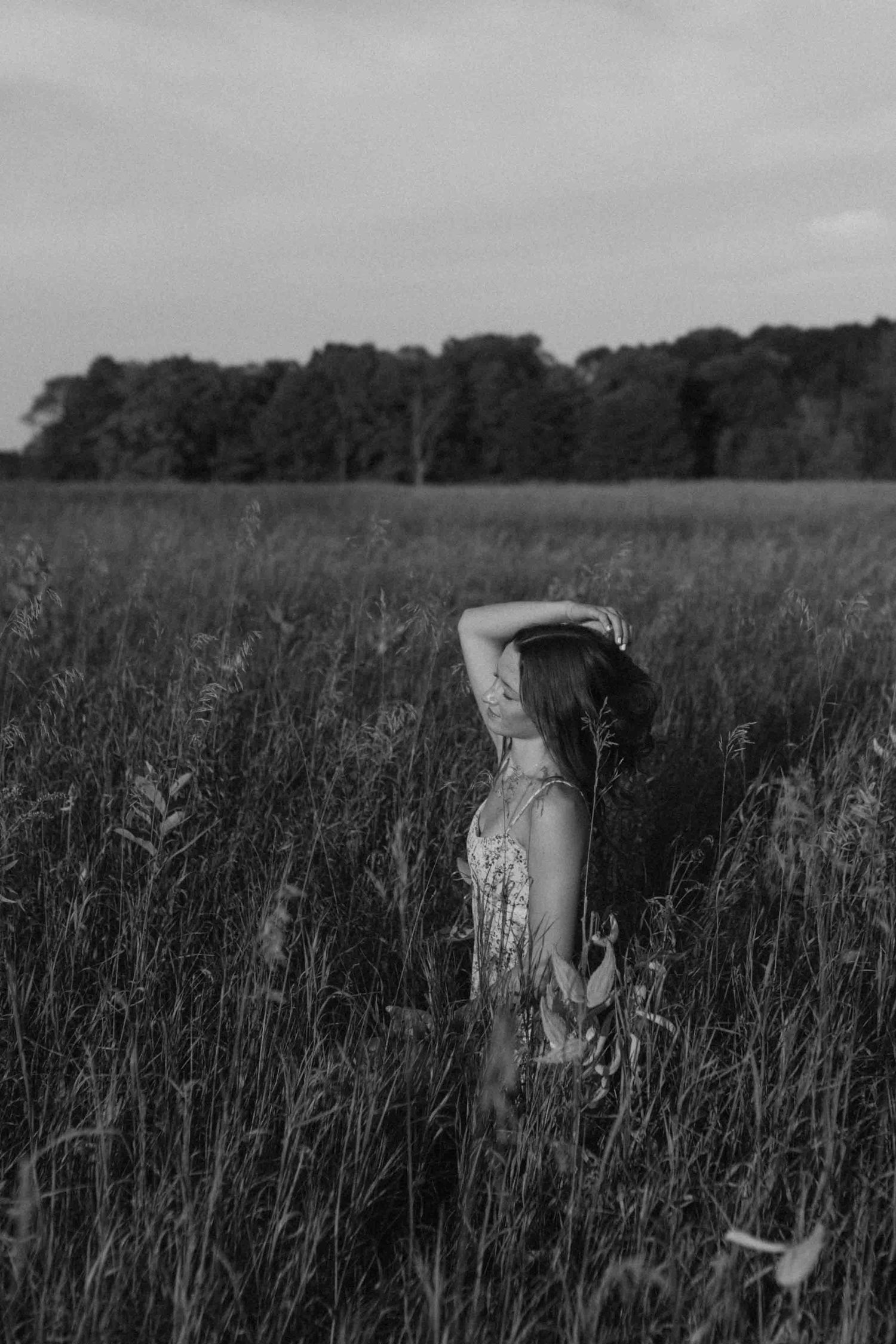 Black and white photo of someone walking through tall grass in a rural field.