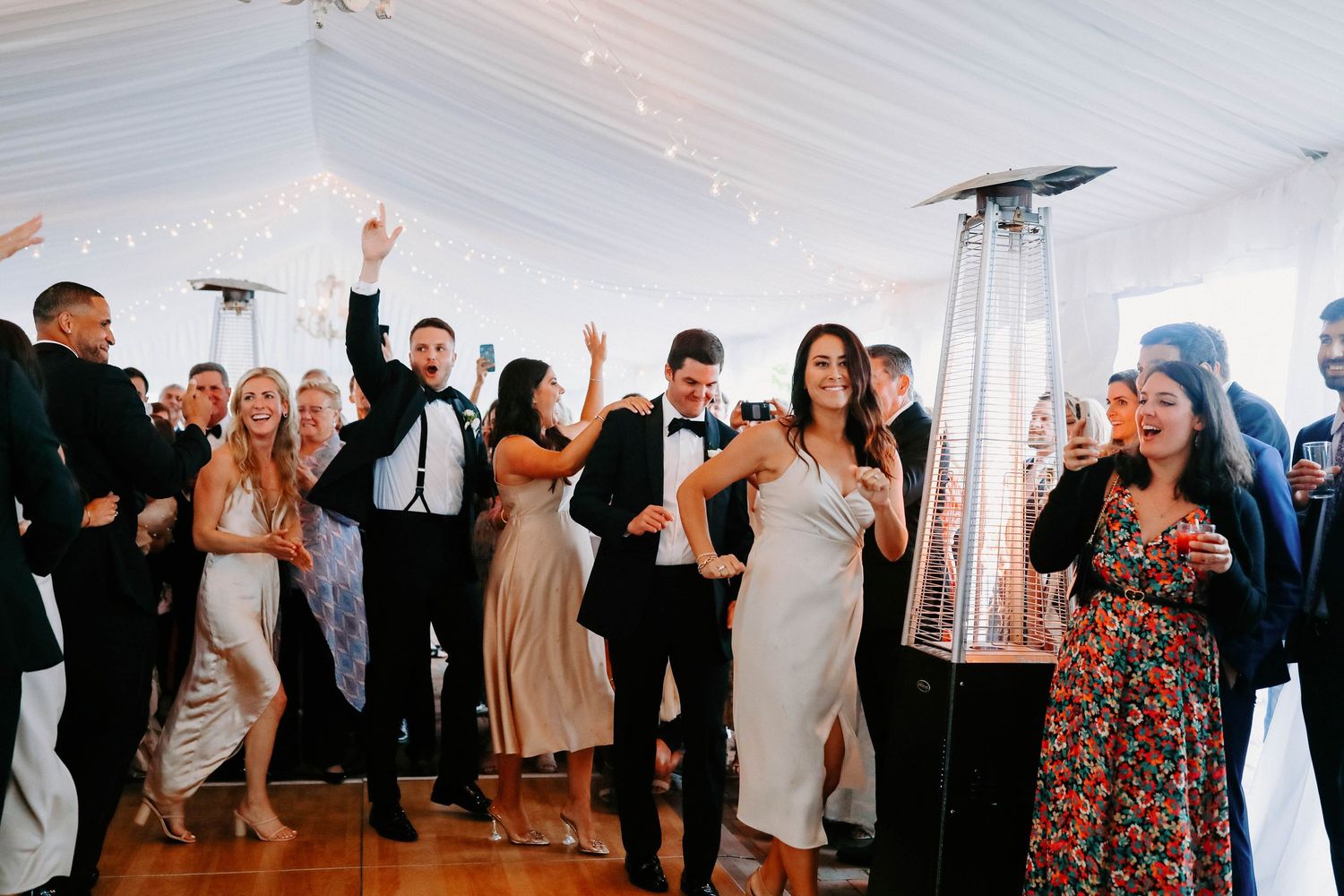 Wedding celebration with guests dancing and celebrating in a white tent venue.