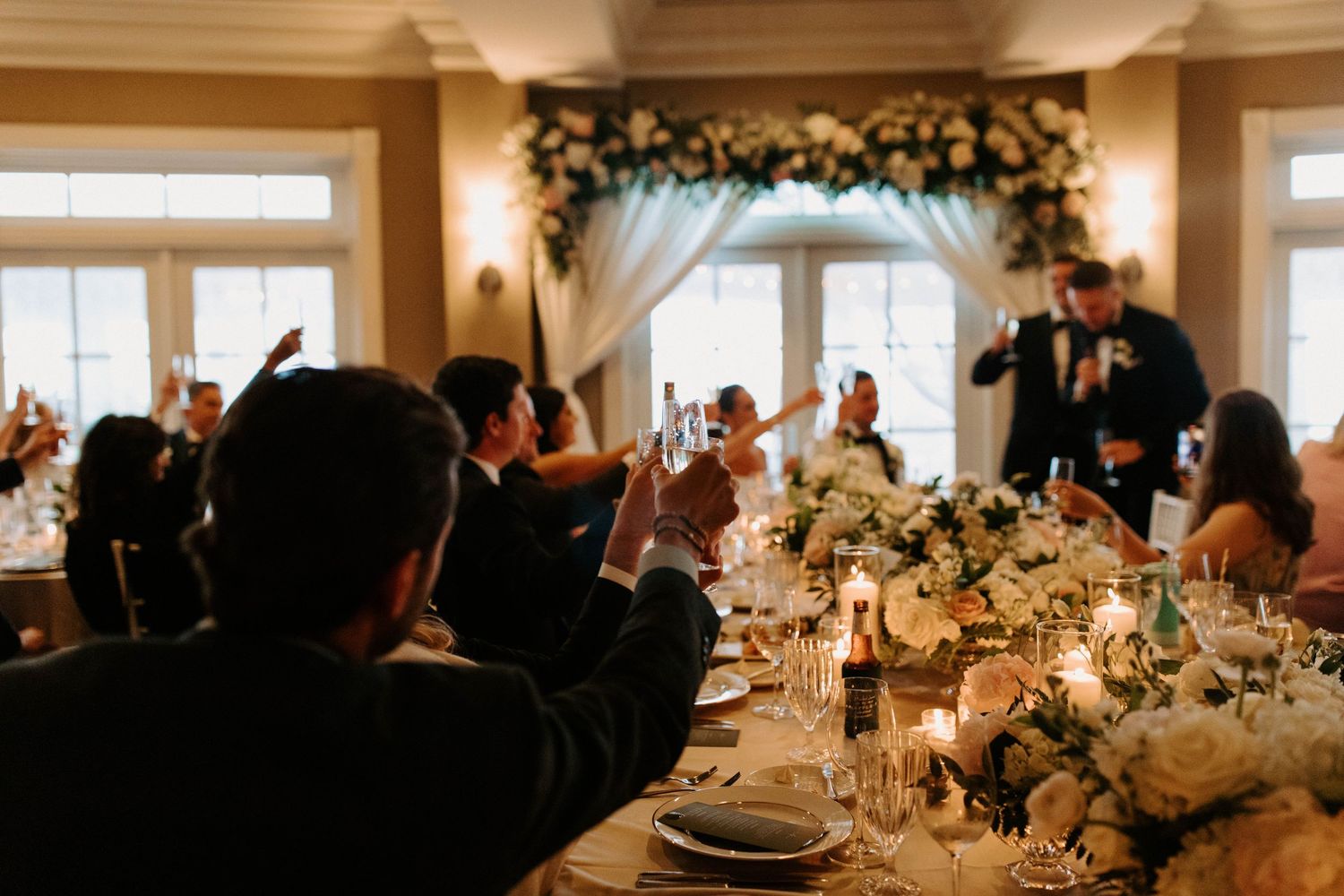 Elegant wedding reception tables decorated with floral centerpieces and candlelight in a bright indoor venue.