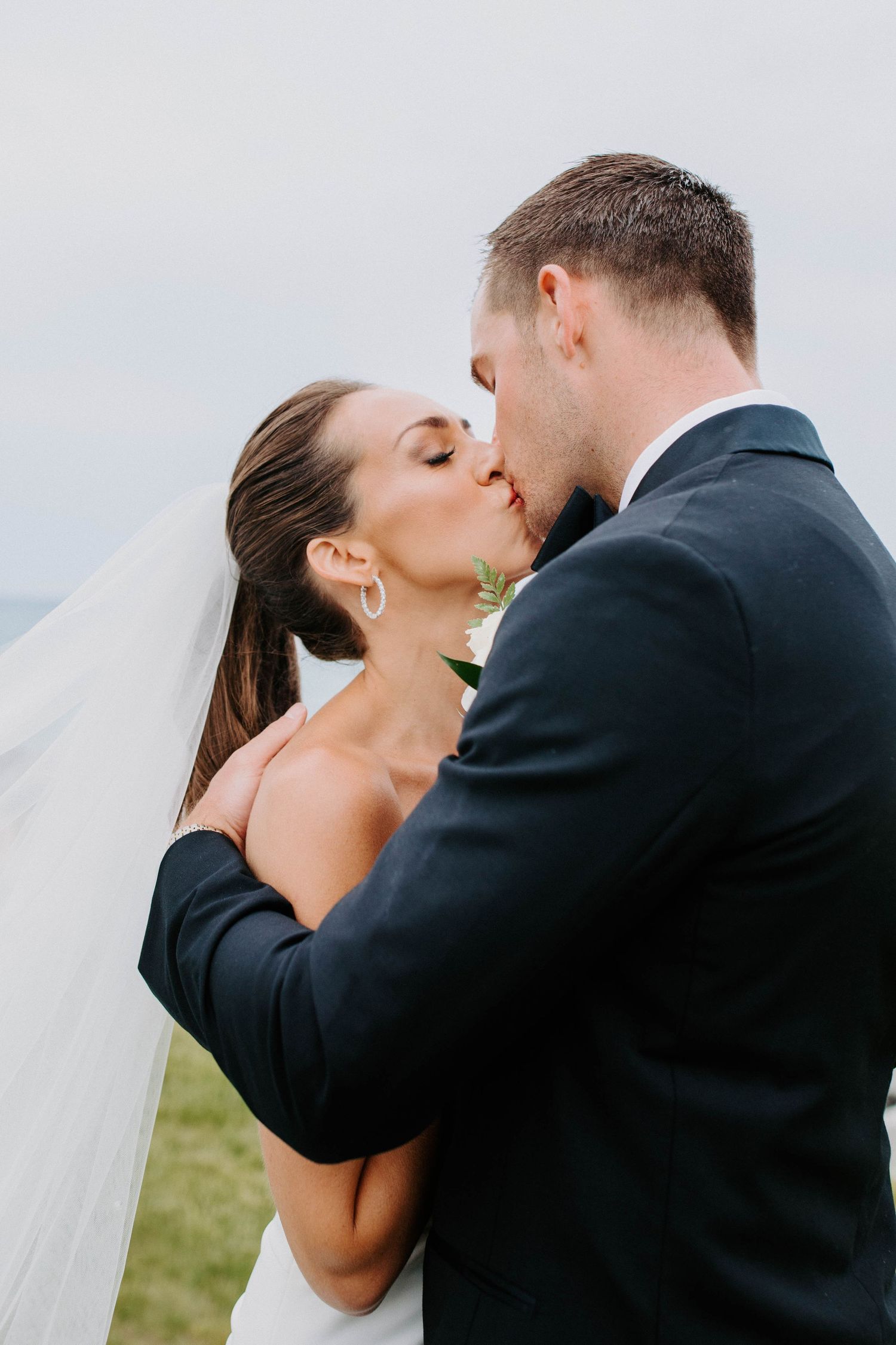 Close-up wedding moment captured against soft sky background.