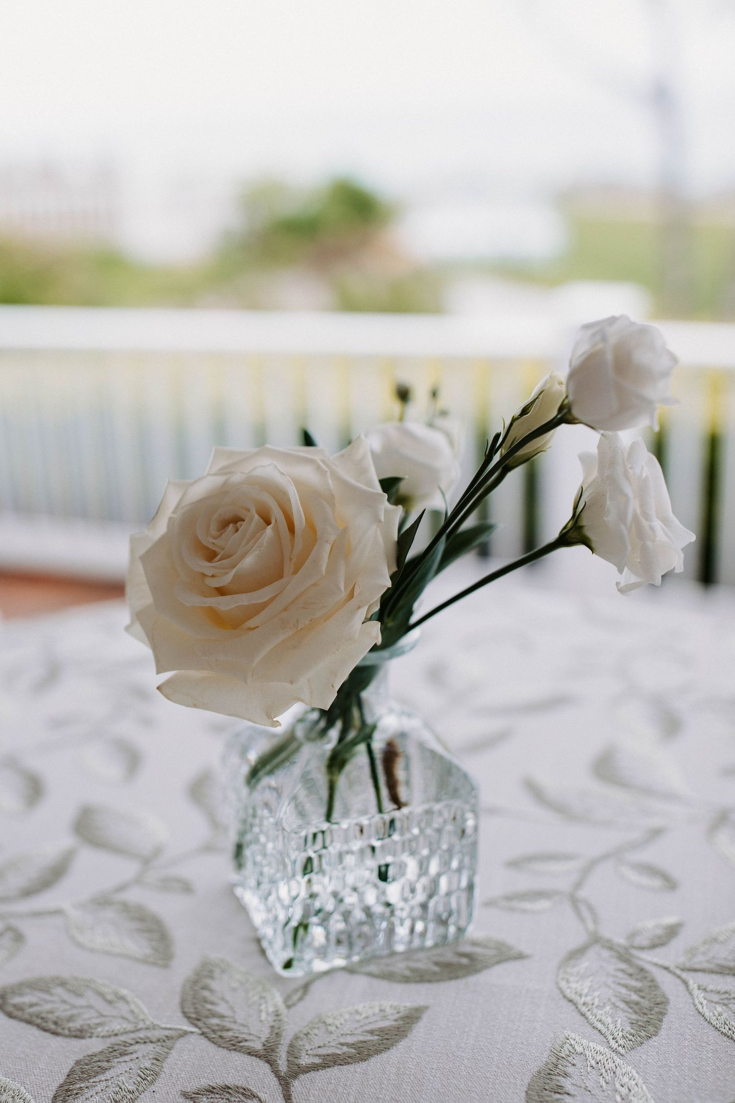 White roses in crystal vases arranged on an embroidered white tablecloth.