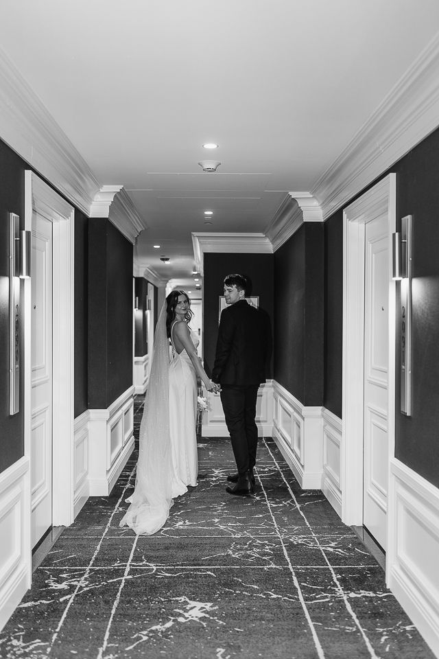 Elegant black and white hallway photos of newlyweds walking through luxury hotel corridor.