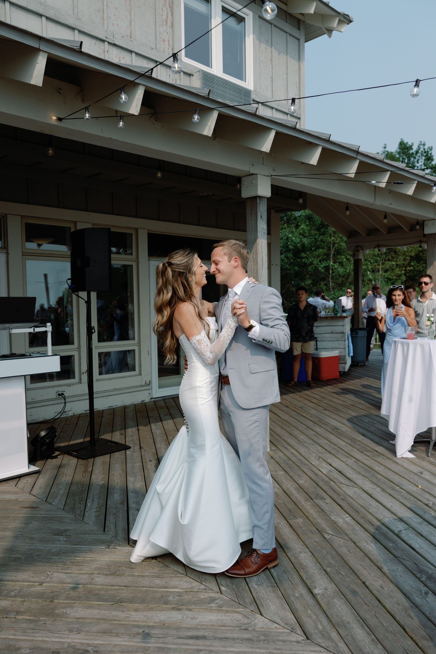Couple dancing together on a wooden deck during their first dance at an outdoor wedding reception.