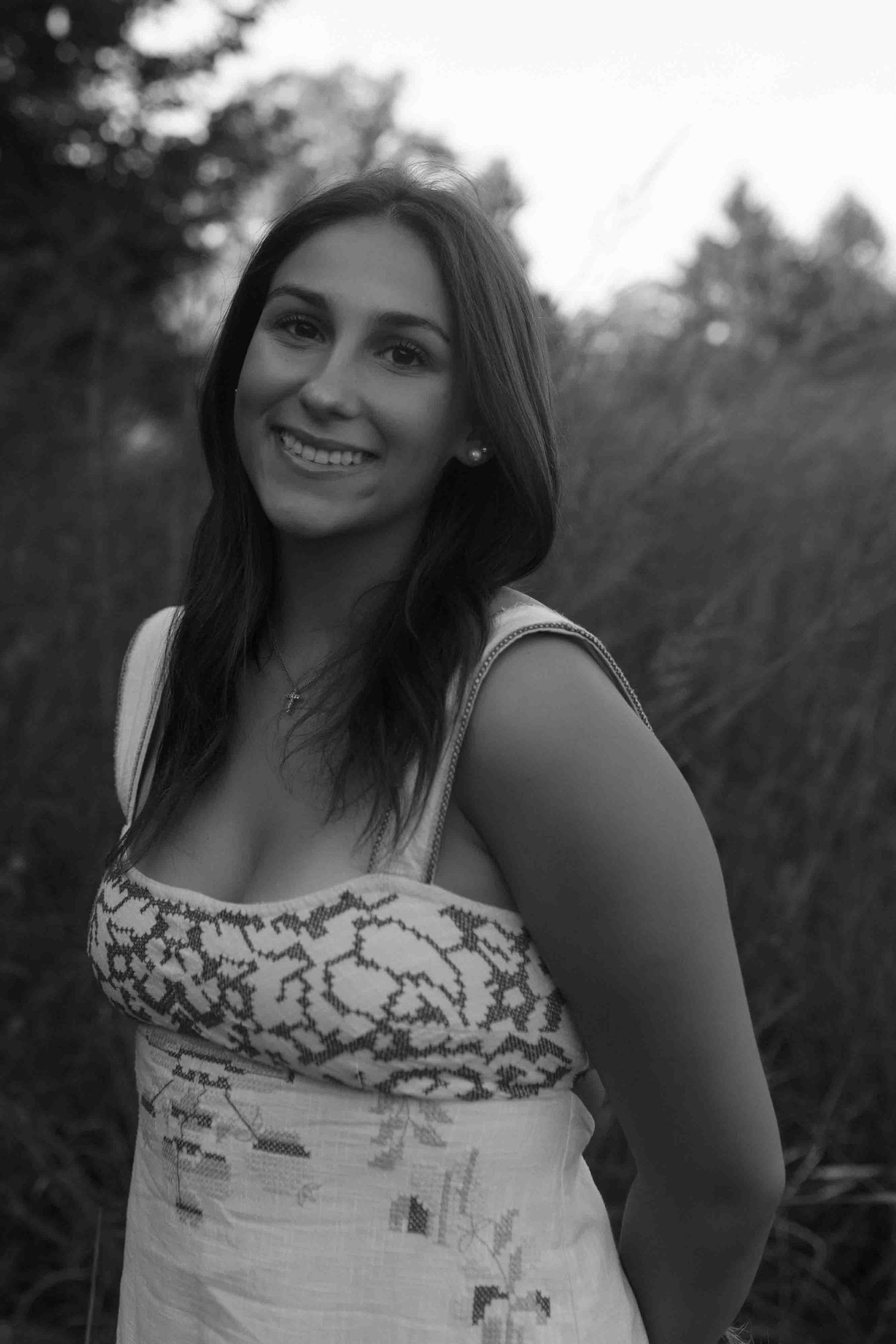 Black and white portrait wearing a white summer top with decorative blue pattern detail.