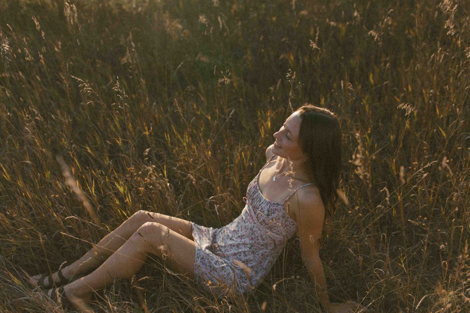 Artistic portrait in a meadow with golden light filtering through tall grass.