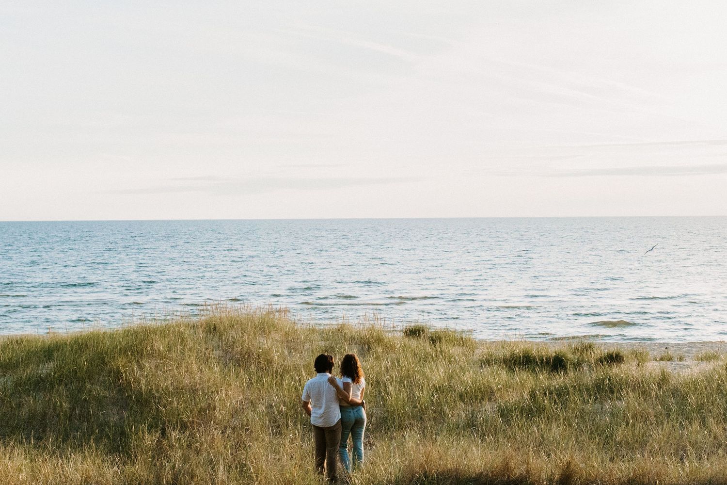 Two silhouettes walk along a peaceful beach at sunset with ocean waves in background.
