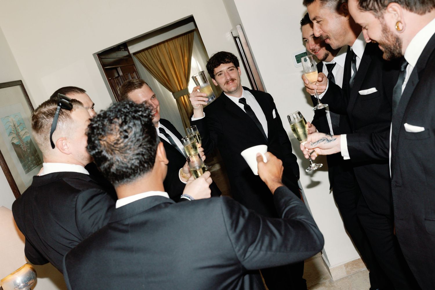Groomsmen in black tuxedos share emotional reactions during a wedding ceremony.