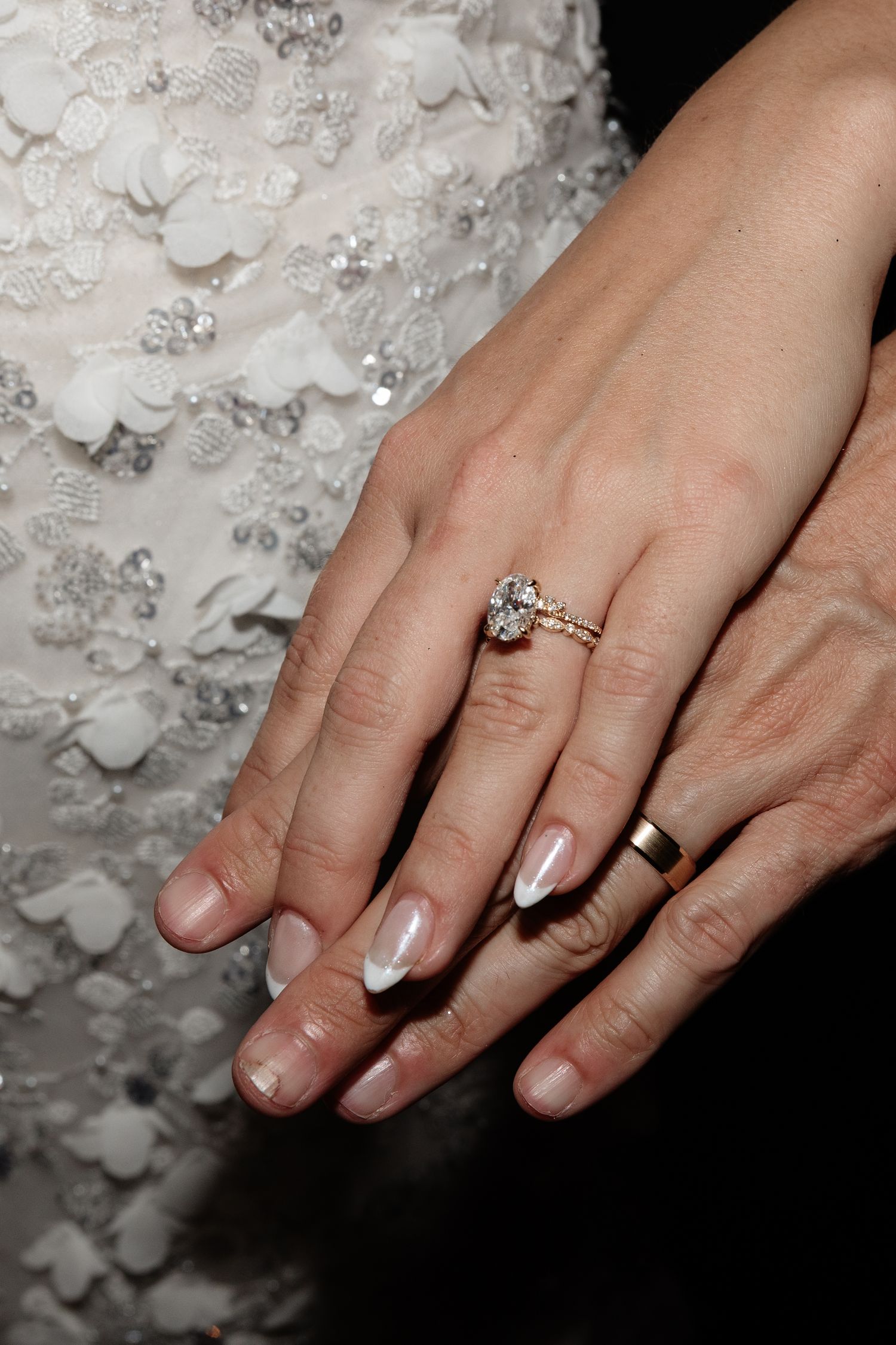 Close-up of bride's hand showing elegant engagement ring and wedding band against lace dress.