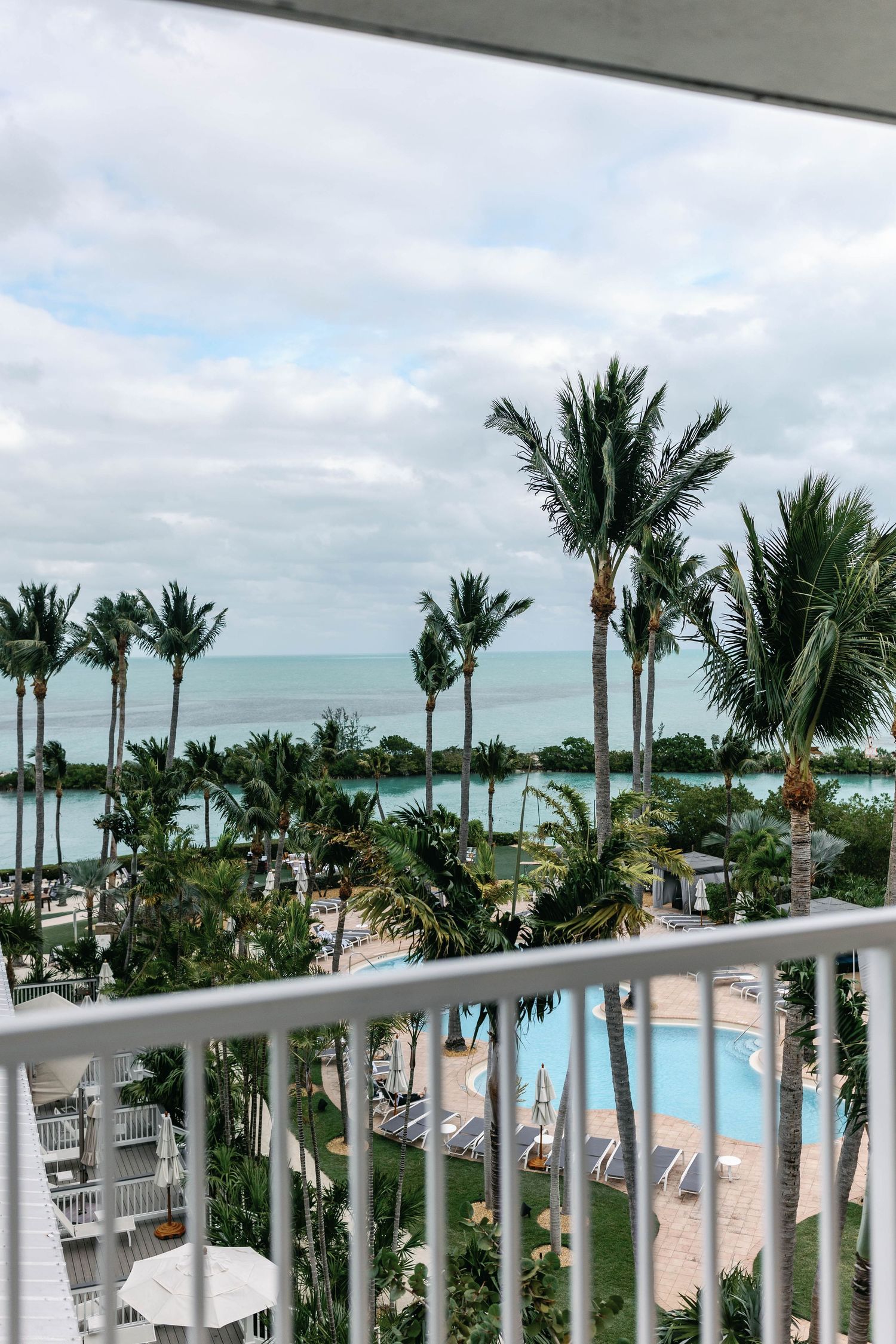 Tropical resort view from balcony showing pool area and palm trees against ocean backdrop.