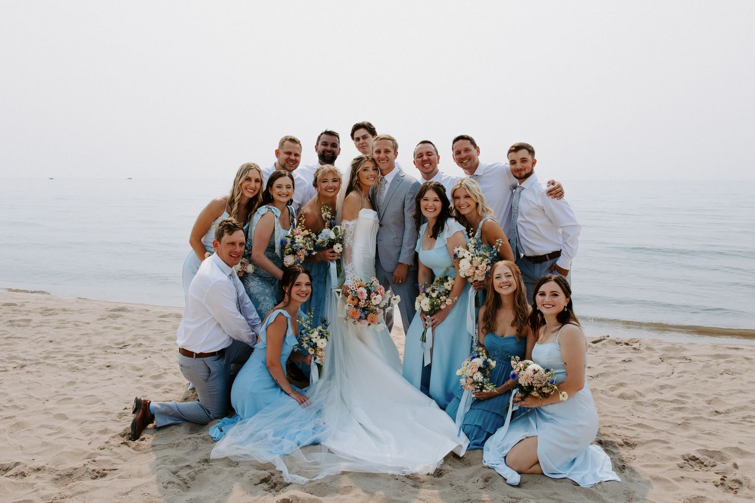 Wedding party gathered on beach in coordinated blue and gray attire.